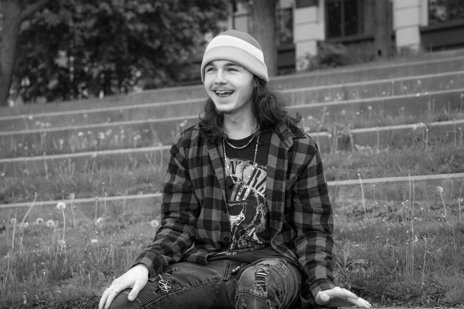 Person in plaid flannel and beanie sitting casually on outdoor steps smiling in black and white photo.