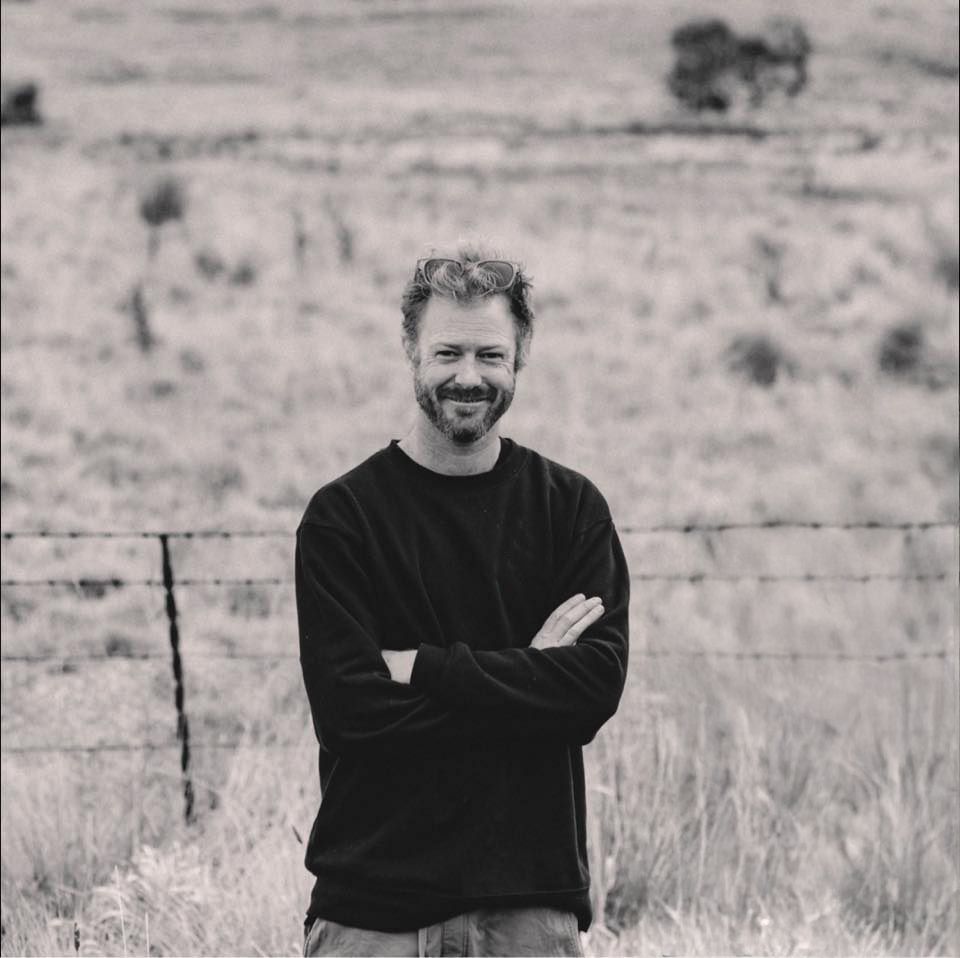 Portrait of photographer in black sweater standing in rural landscape.