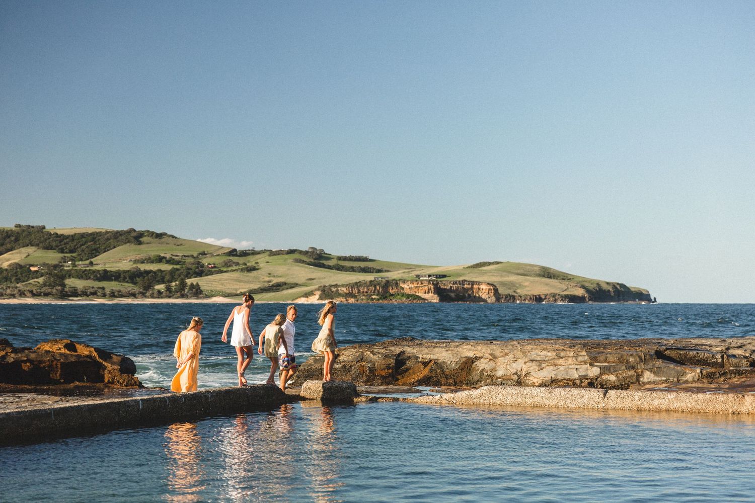 Family walking on rocky coastal pools in Gerringong during sunset by the ocean.