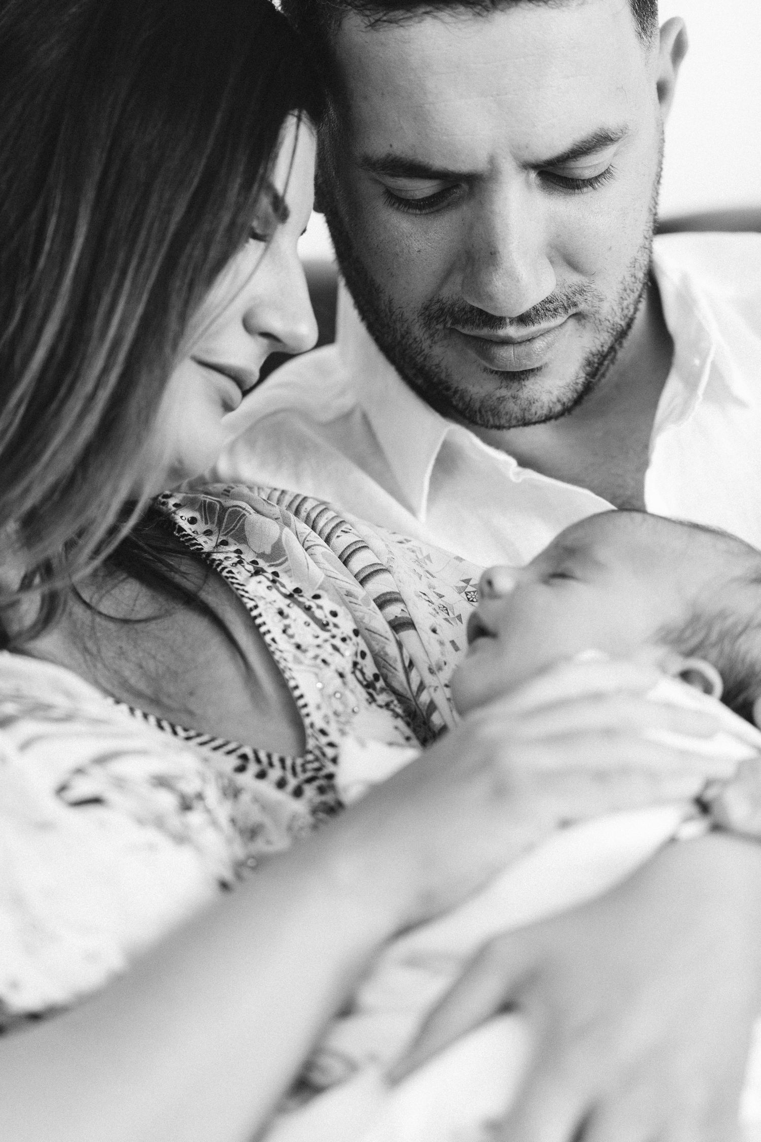 Parents lovingly gaze at their newborn baby in an intimate black and white portrait. Oak Flats