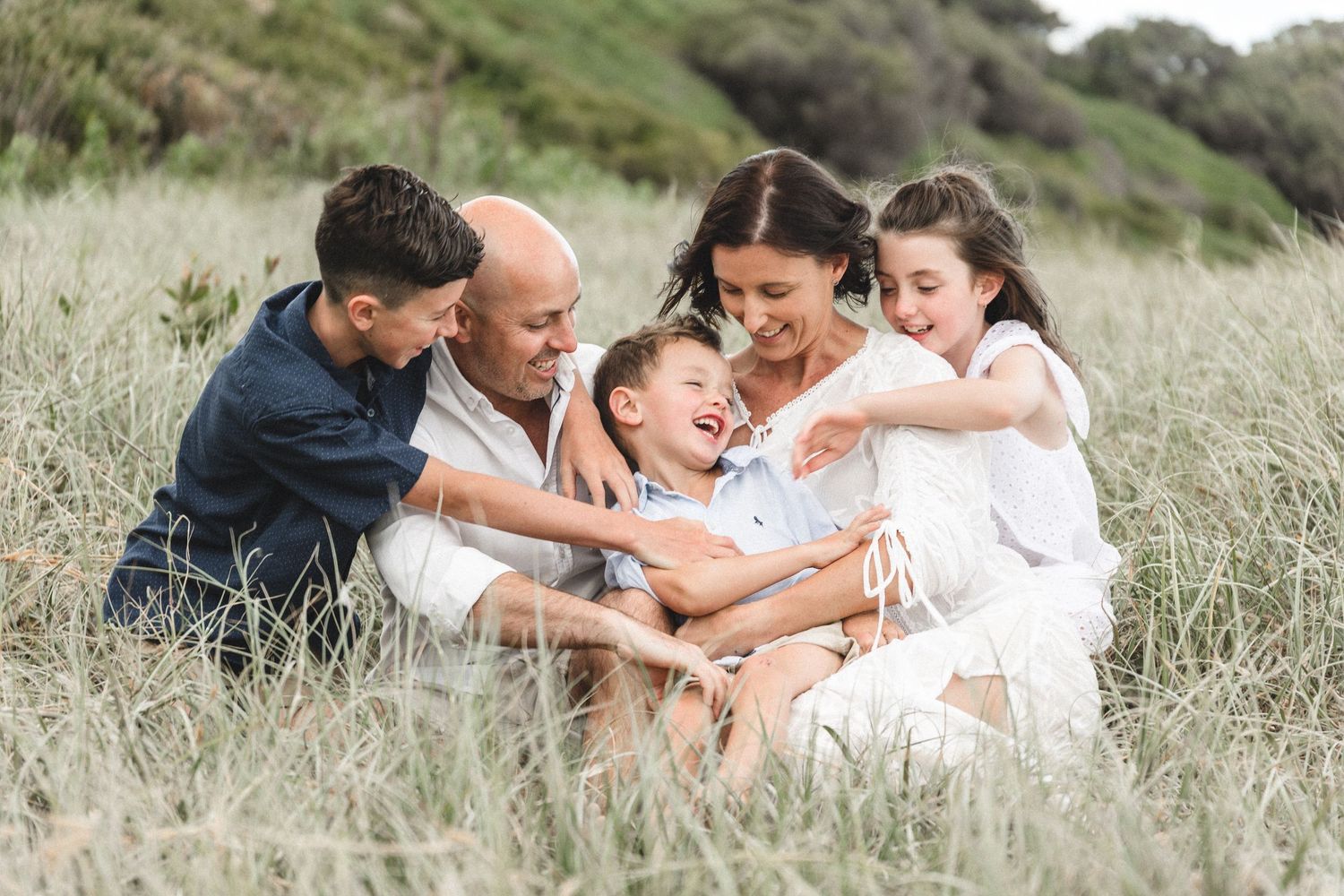 Family sharing joyful moment together while sitting in tall grass field. Port Kembla