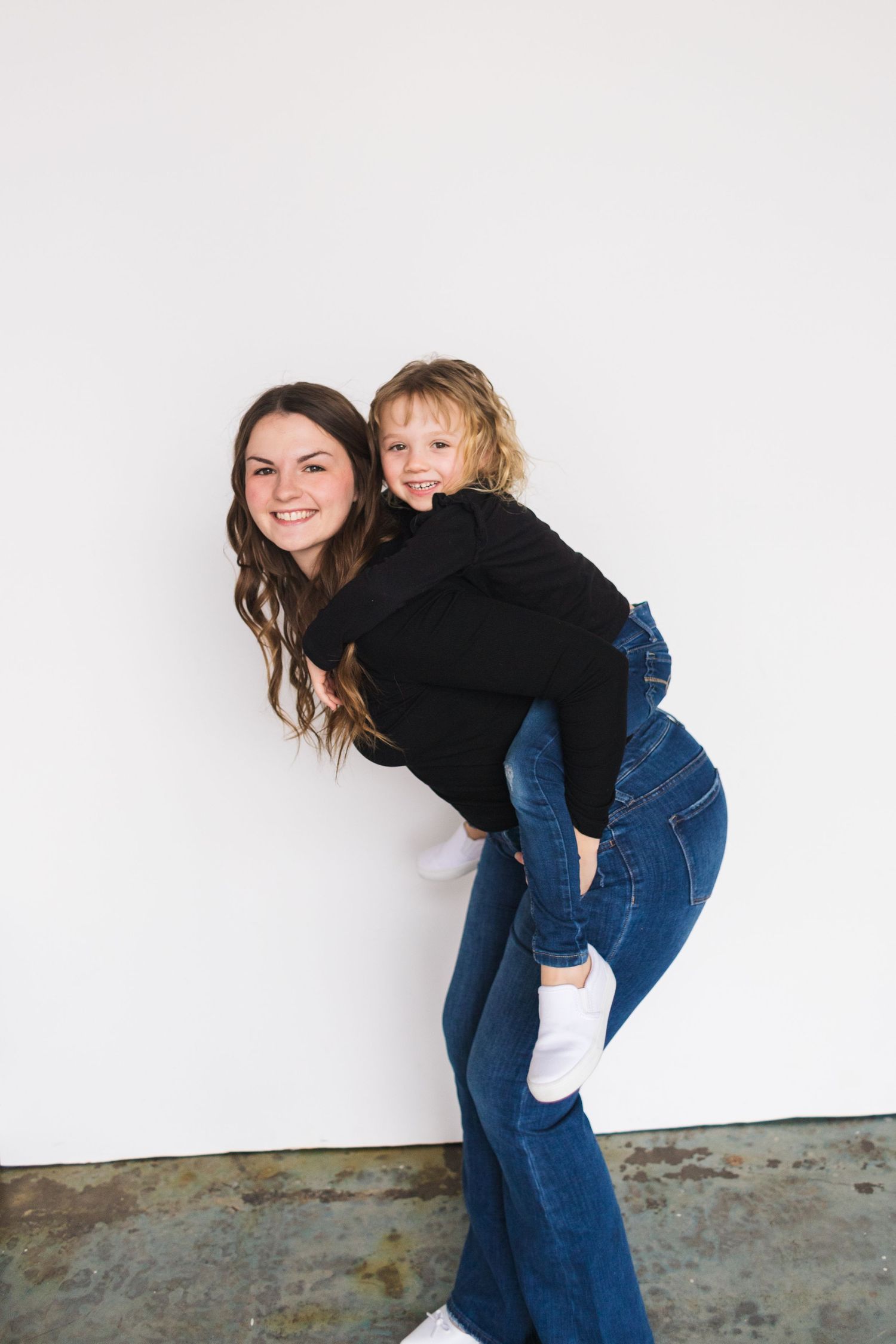Playful mother and child interaction against white wall wearing matching outfits.