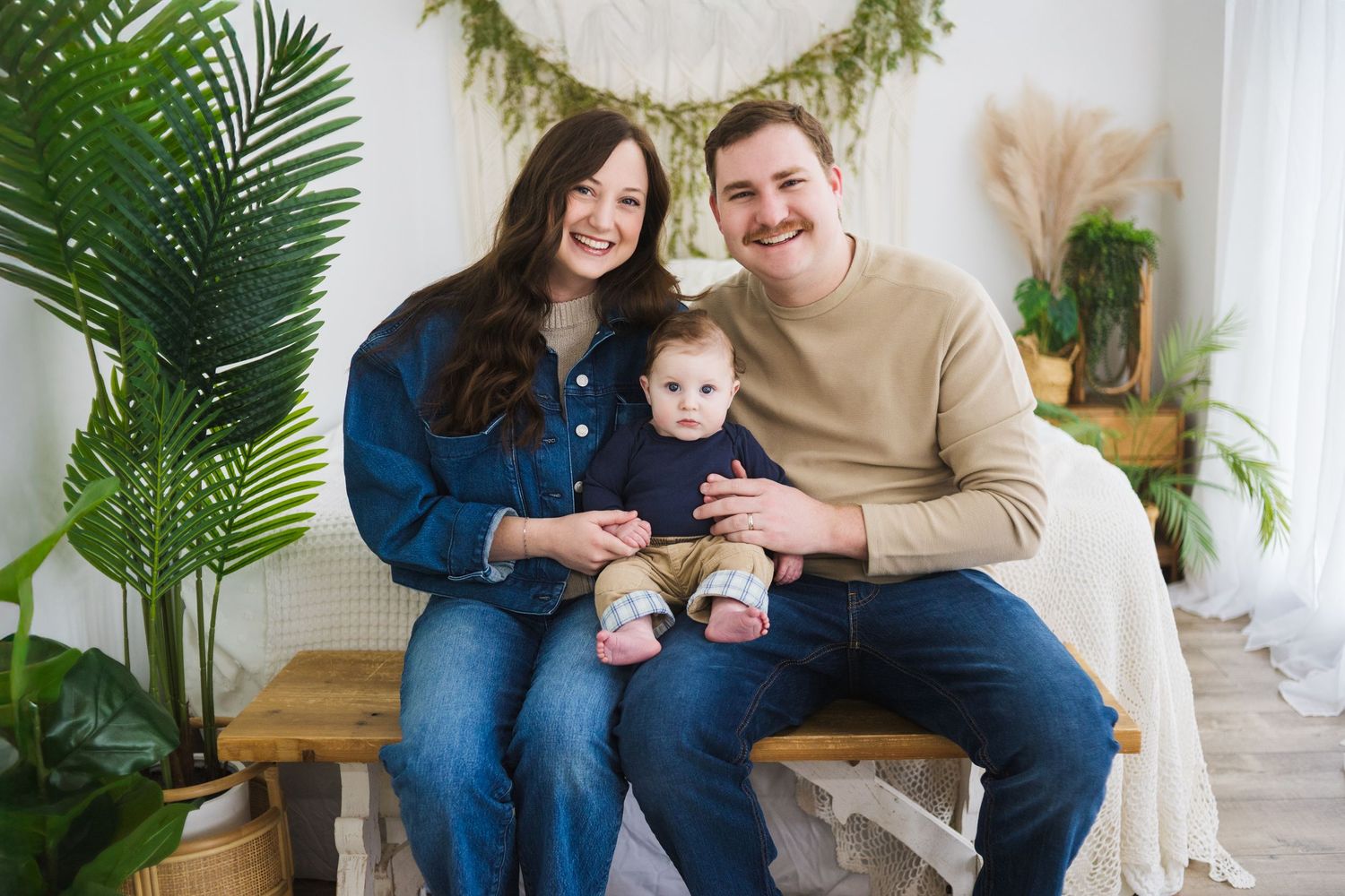 Family portrait with greenery garland and tropical palm leaves in bright studio setting.