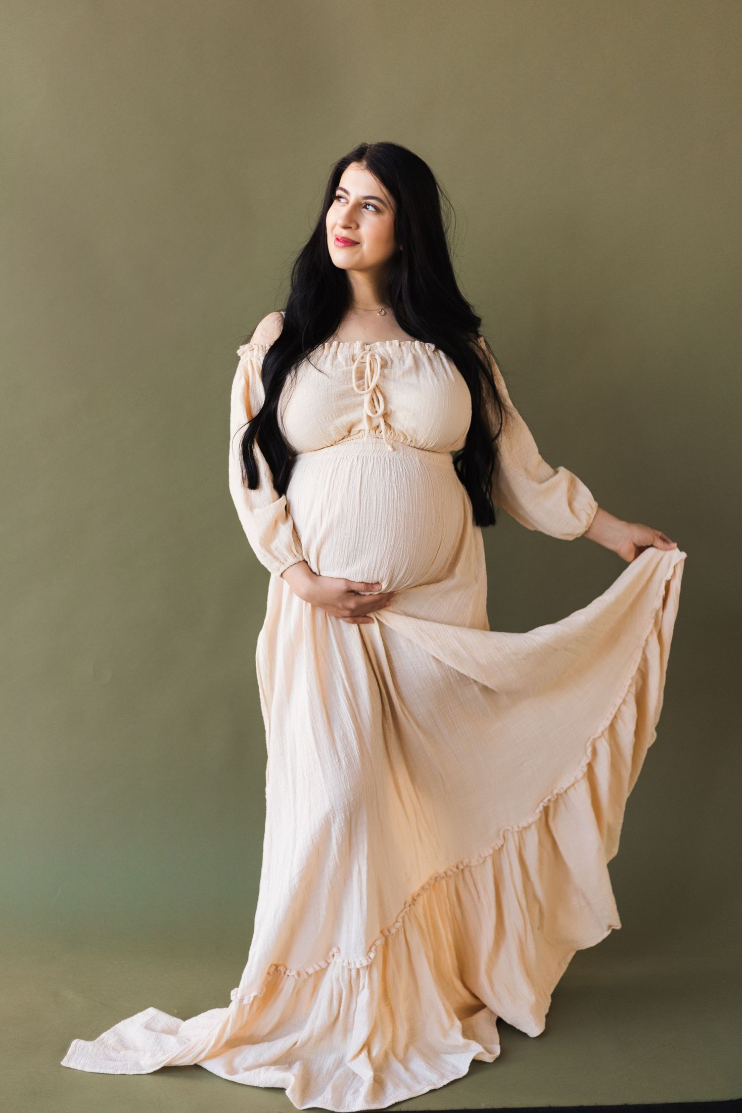 A flowing cream maternity dress creates elegant movement in studio portraits.