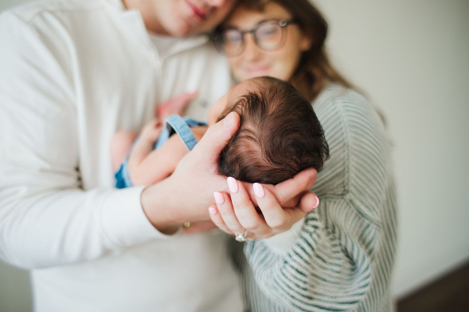 Parents tenderly cradling their newborn baby together, close-up of infant's head in loving hands.