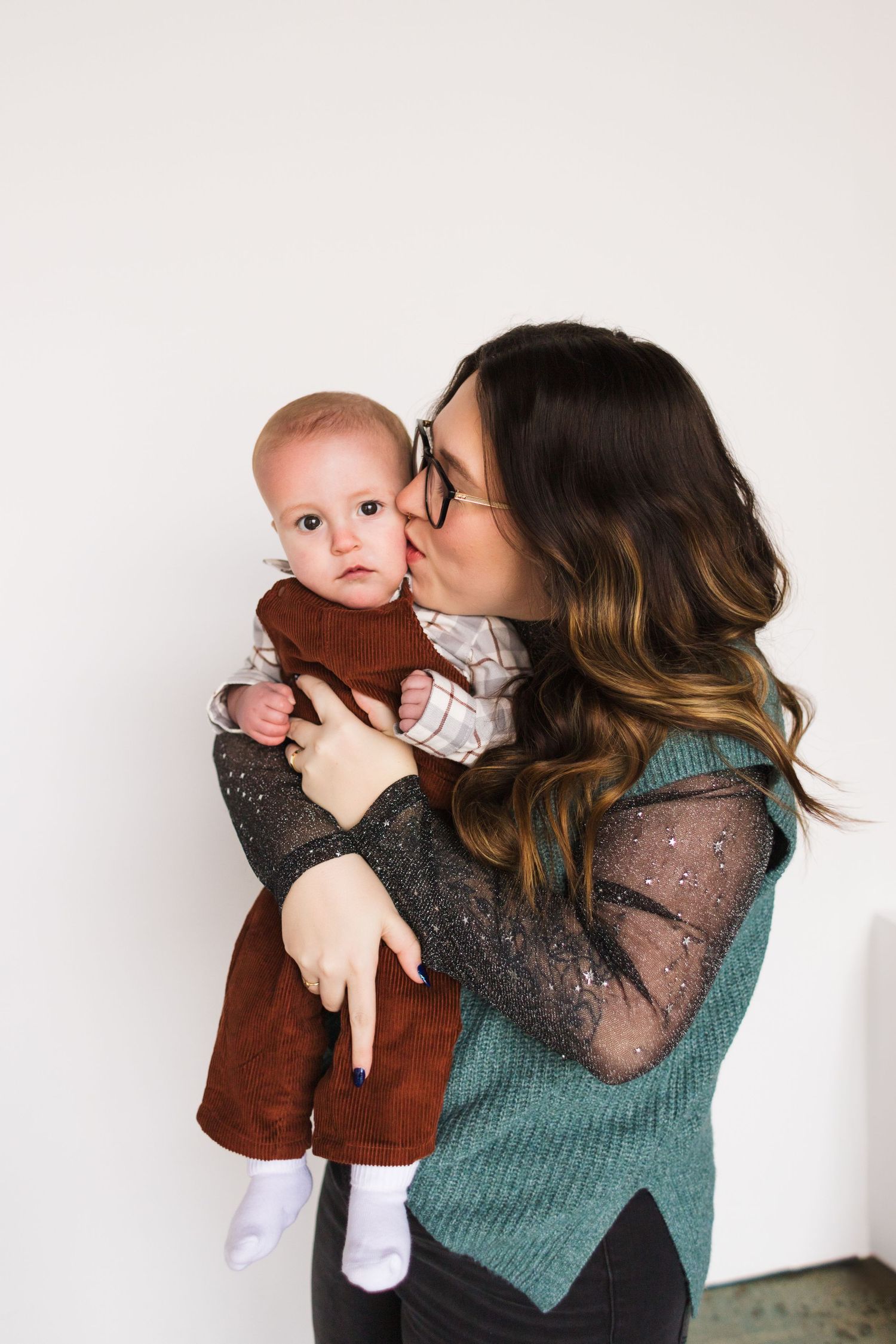 Parent in teal sweater showering affection on baby in brown outfit.