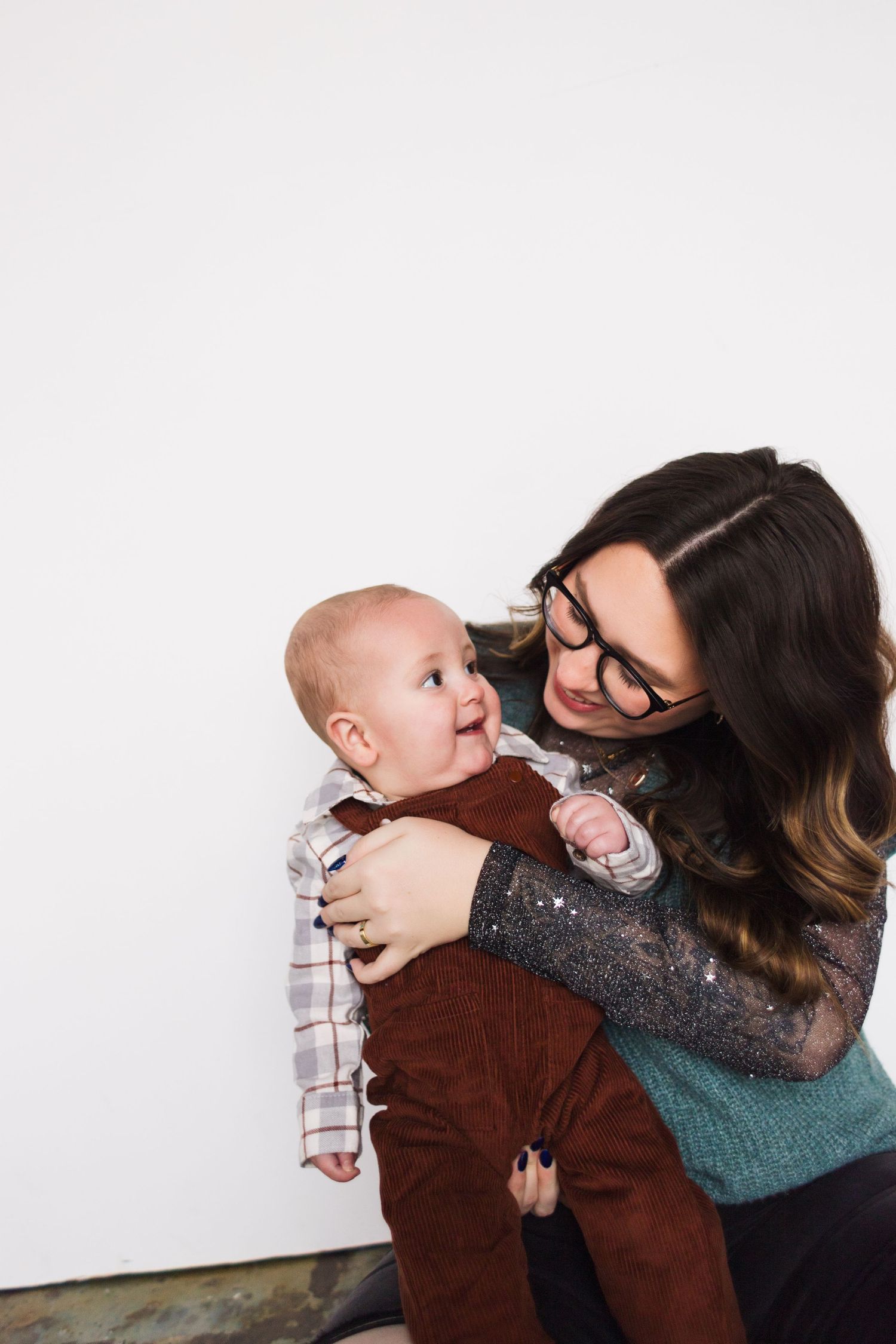 A tender moment between parent and baby wearing a brown corduroy outfit against a white background.