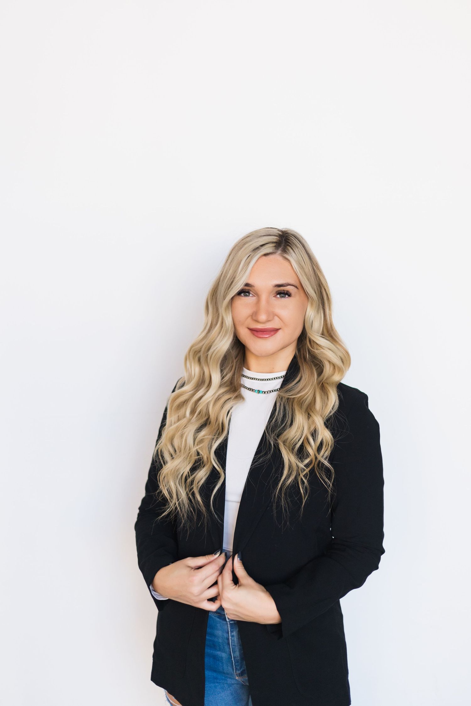 Stylish woman in business attire smiles against white backdrop.