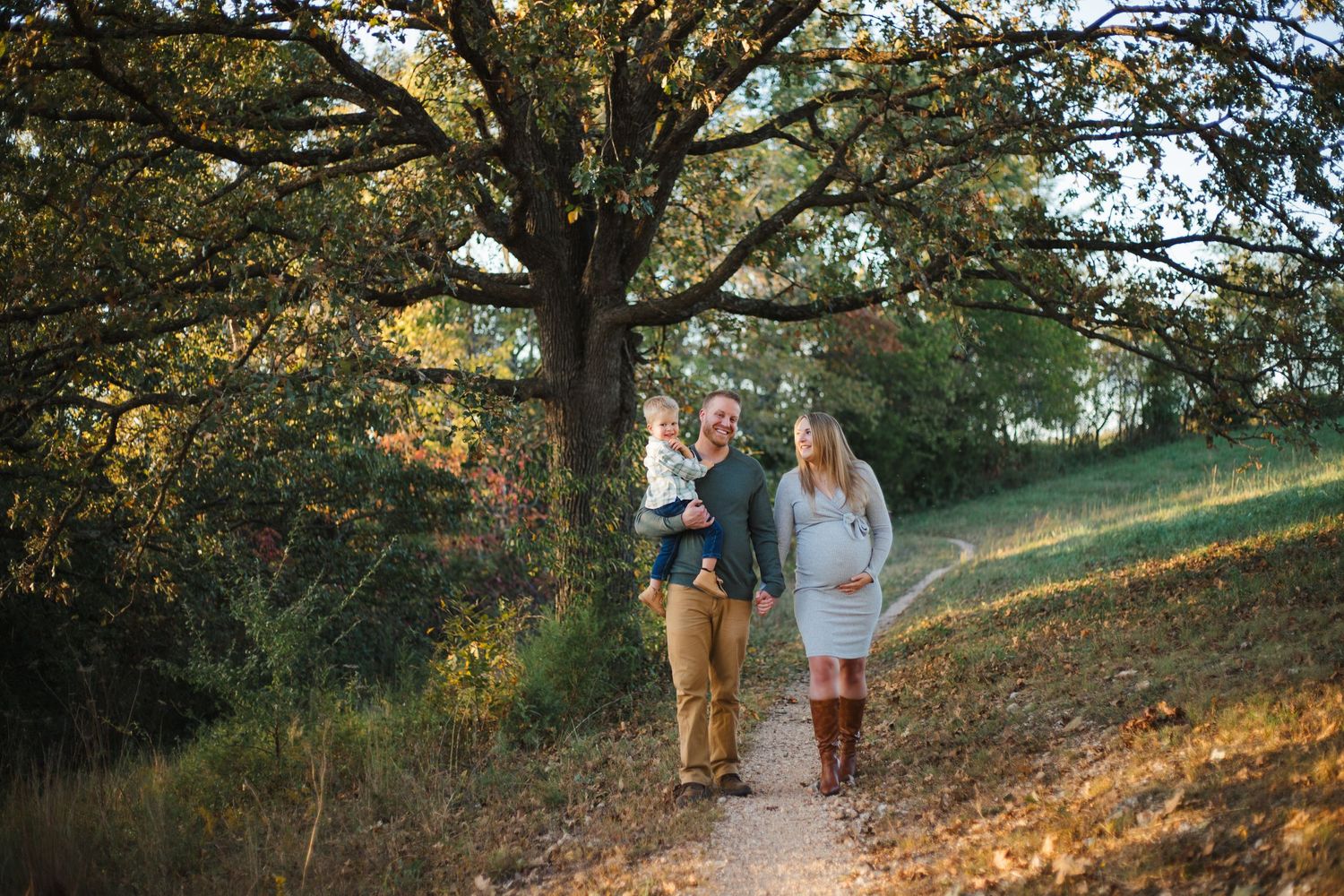 A couple walks together on a scenic wooded path during golden hour sunlight.