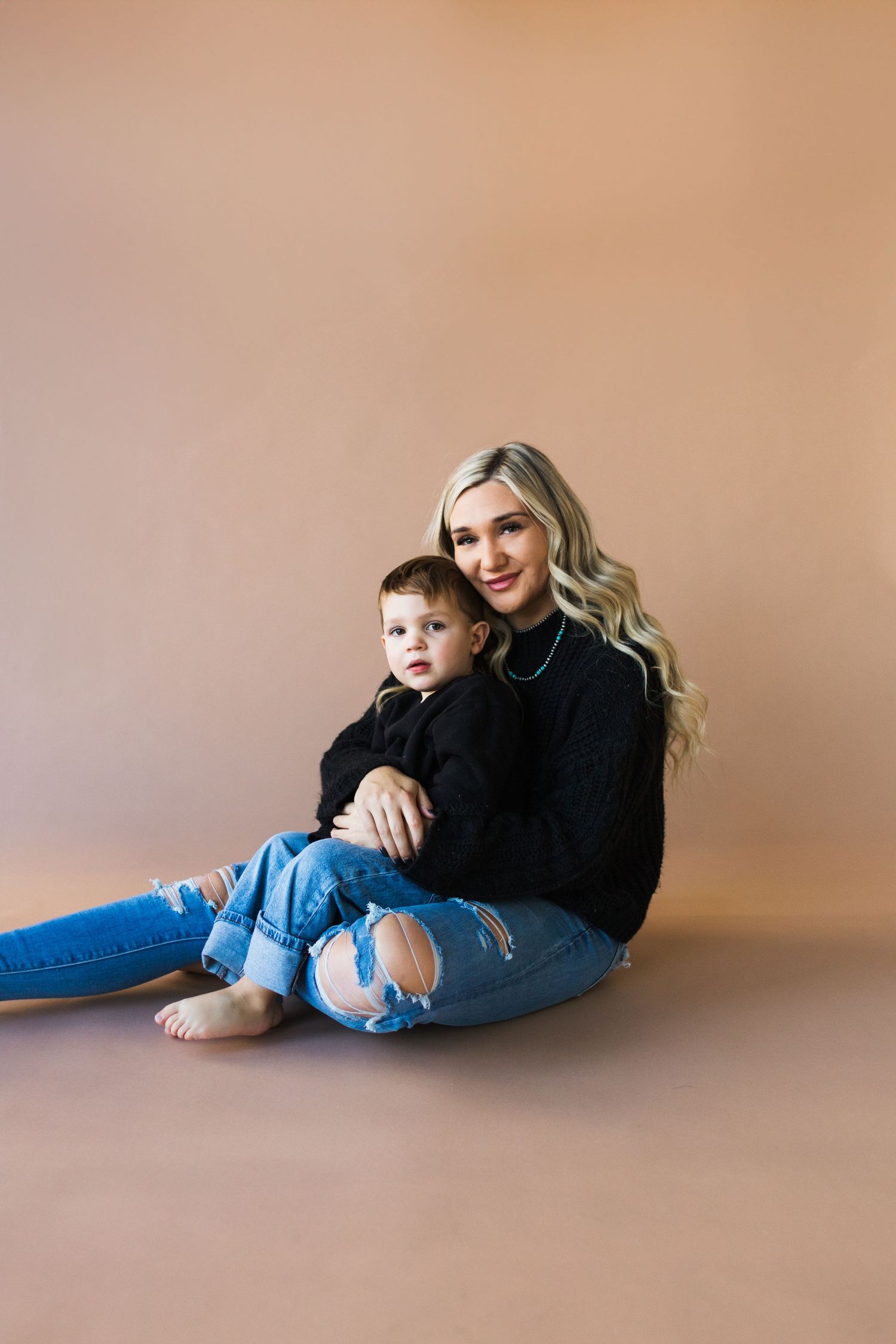 Parent and child in matching black tops and jeans pose on brown backdrop.