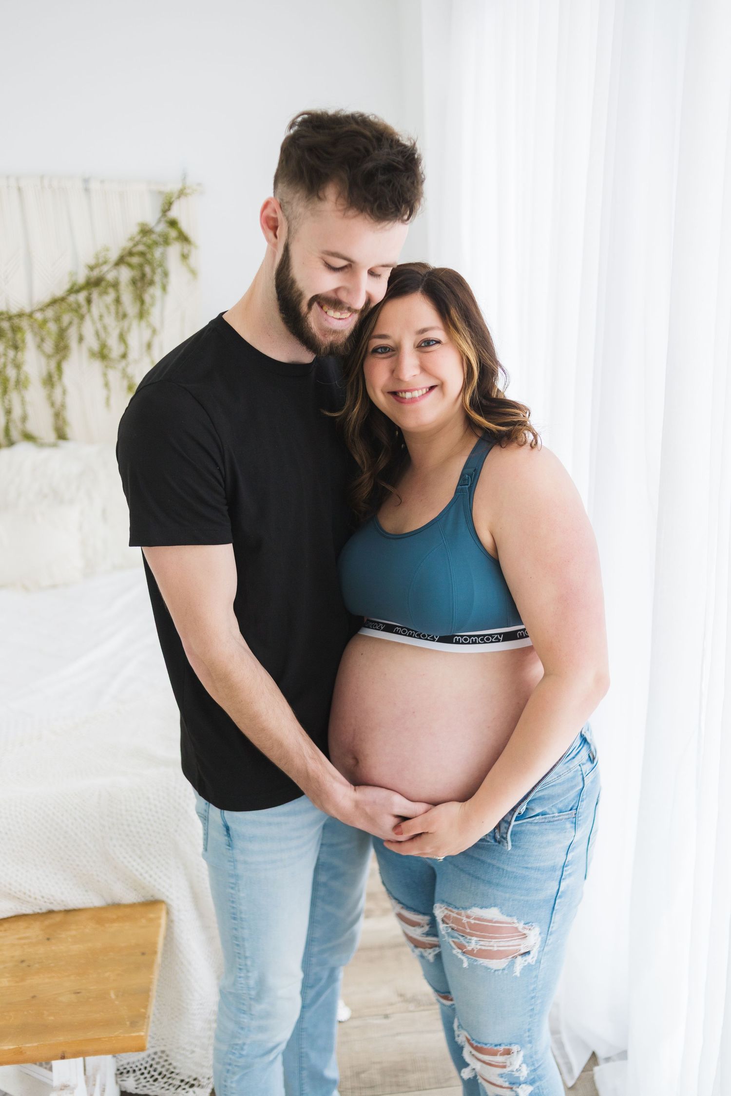 A couple shares an intimate moment during their maternity photoshoot in a bright indoor setting.