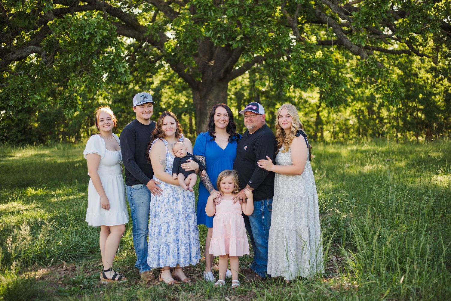 A group wearing coordinating blue and white outfits poses for outdoor family photos in a lush green summer setting.