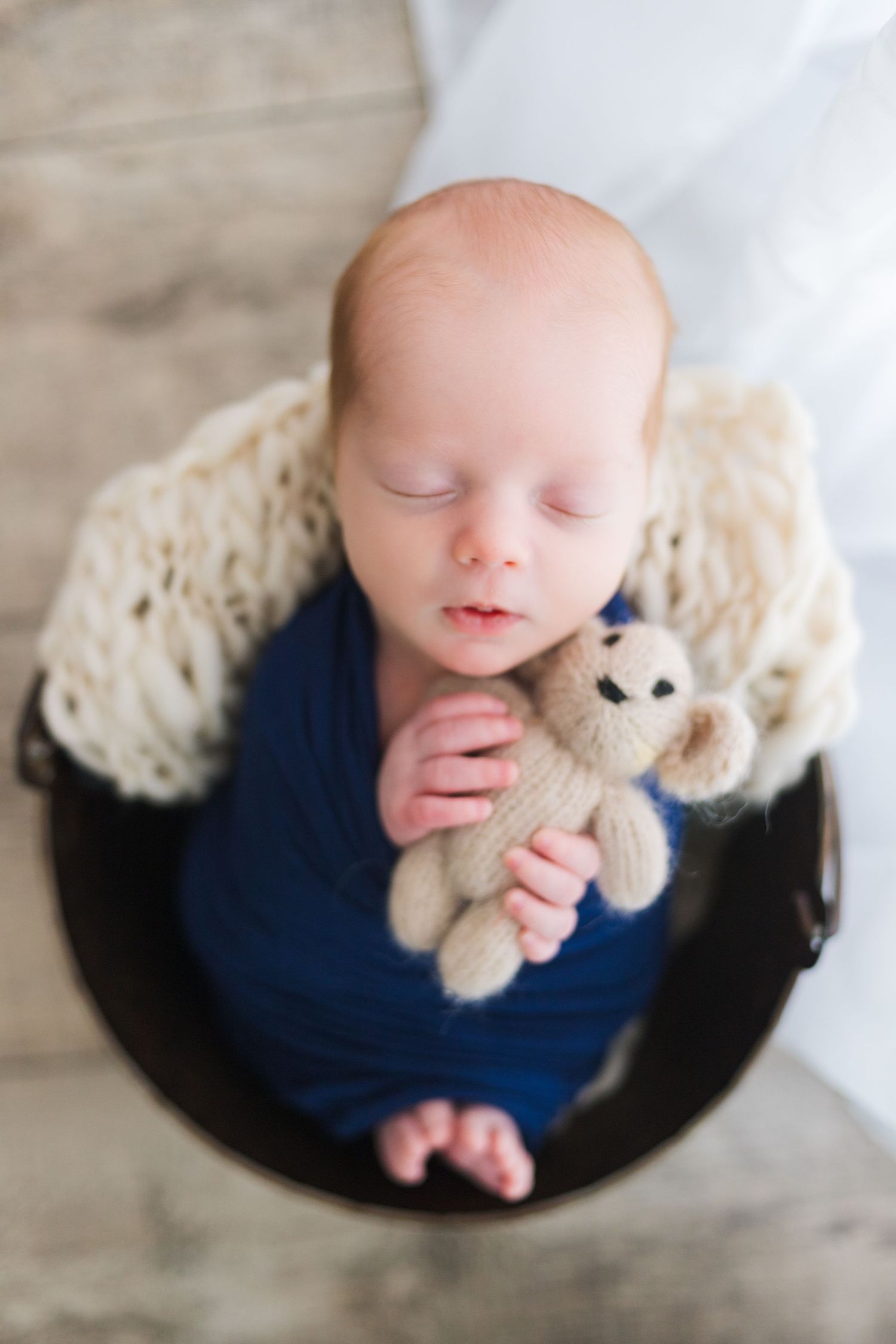 Newborn posed safely in navy blue wrap with cream layer in bucket – Springfield MO studio photographer