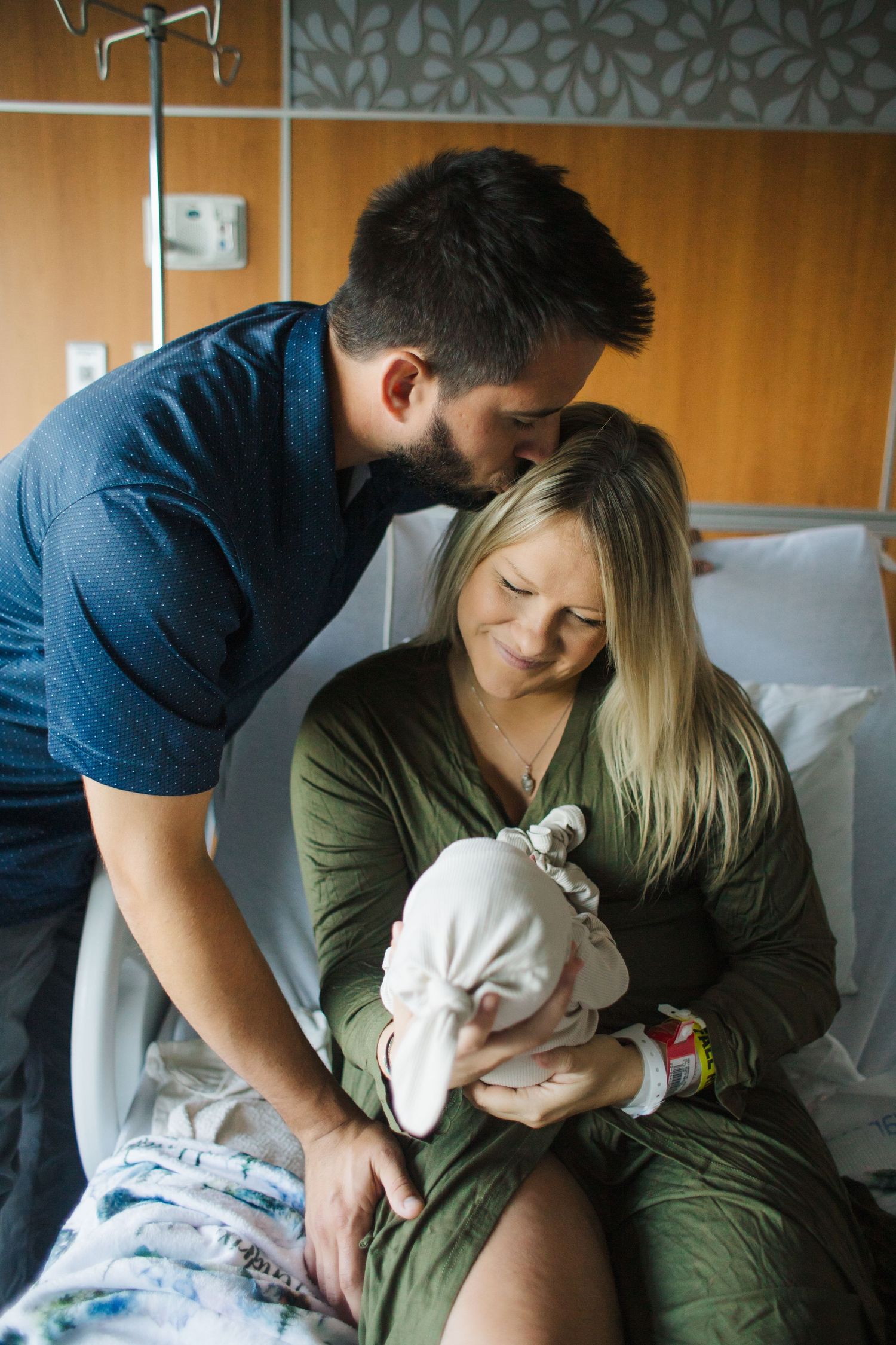 A couple sits together on a hospital bed sharing tender moments with their newborn baby.