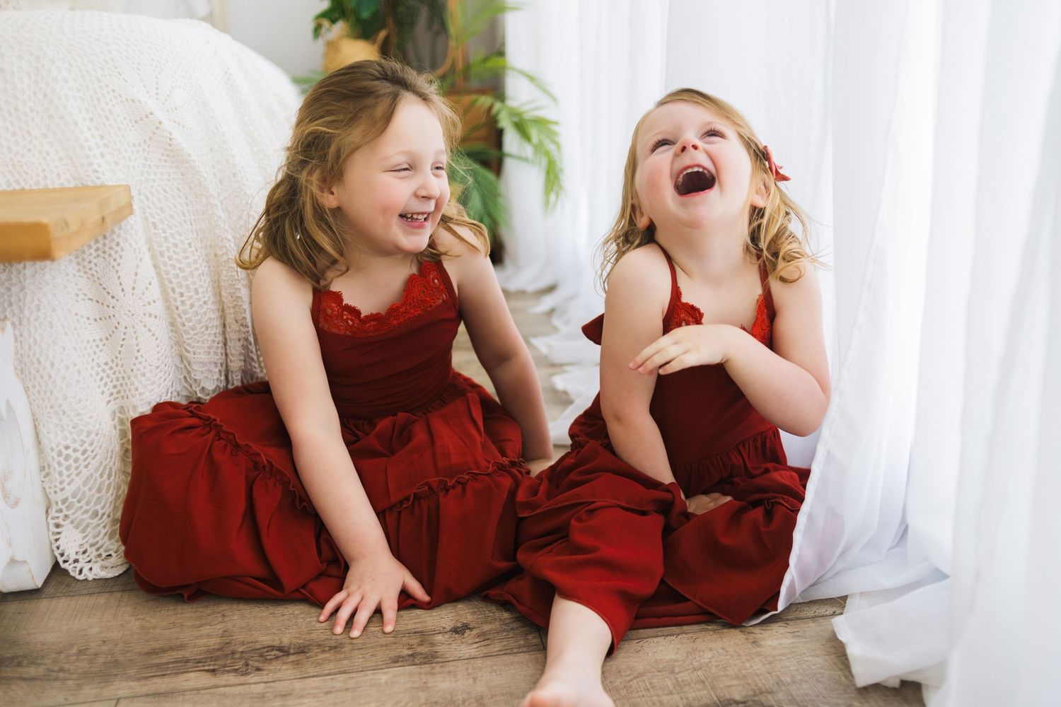 Children in burgundy dresses sharing playful moments during family photography session.