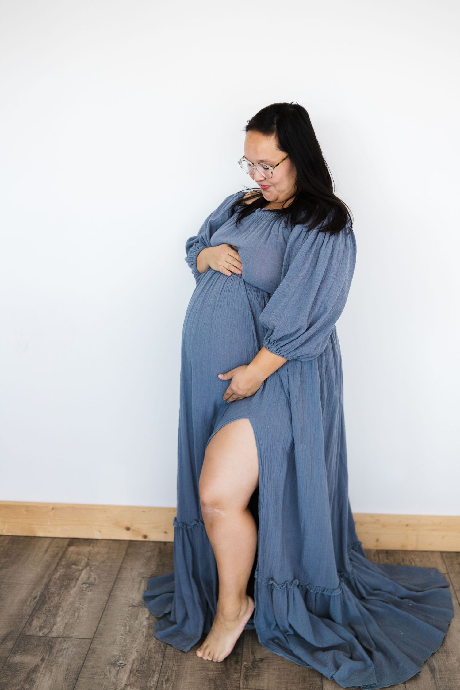 Artistic maternity photos in flowing blue dress against white studio backdrop.