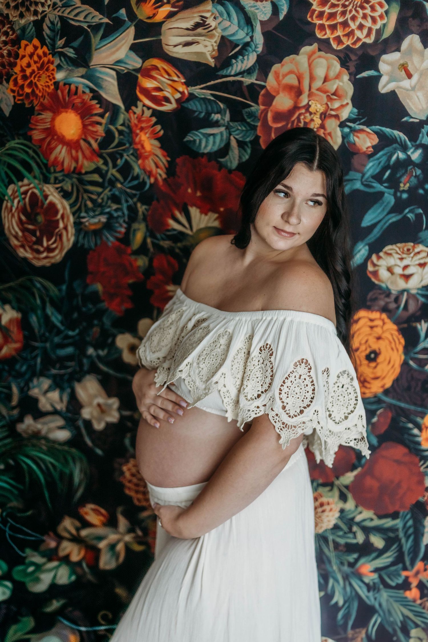 Elegant maternity portrait against dark floral wallpaper with orange and pink blooms.