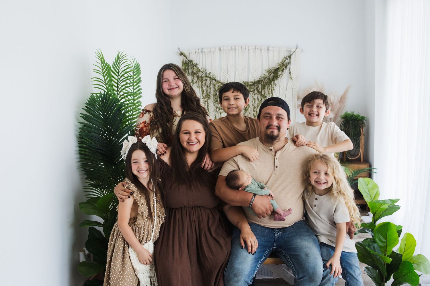 Family photo in white studio setting with plants and bohemian decor elements.