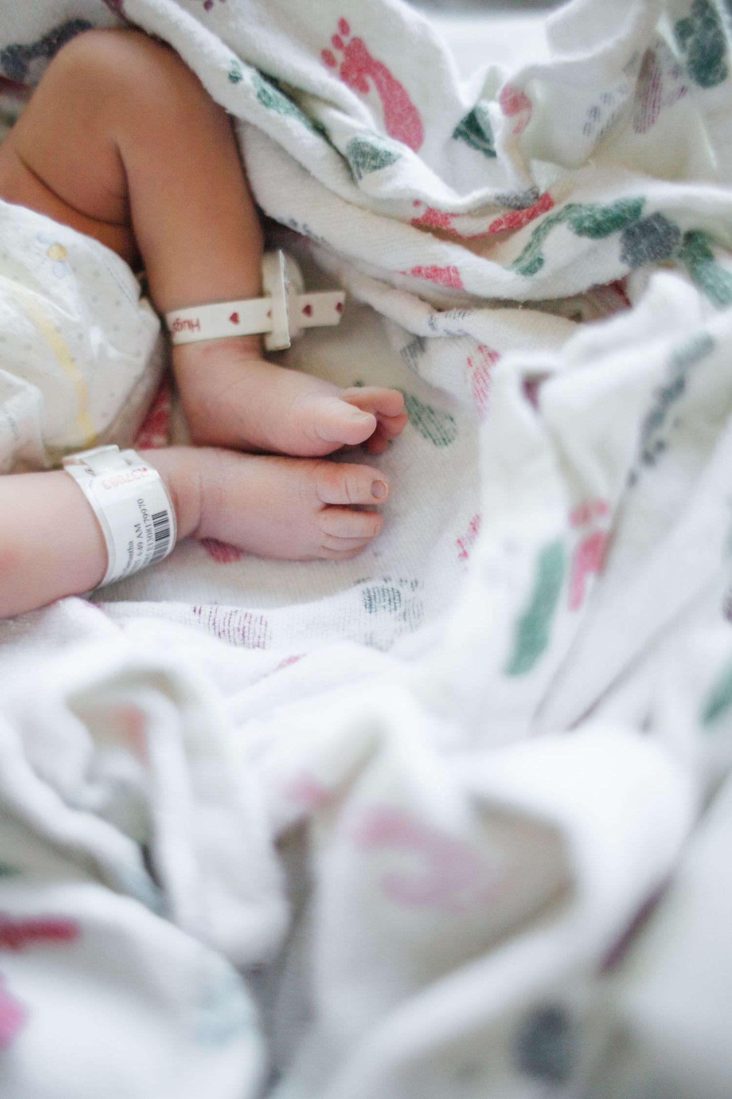 Close-up of tiny newborn feet with hospital ID bracelet on white floral blanket.
