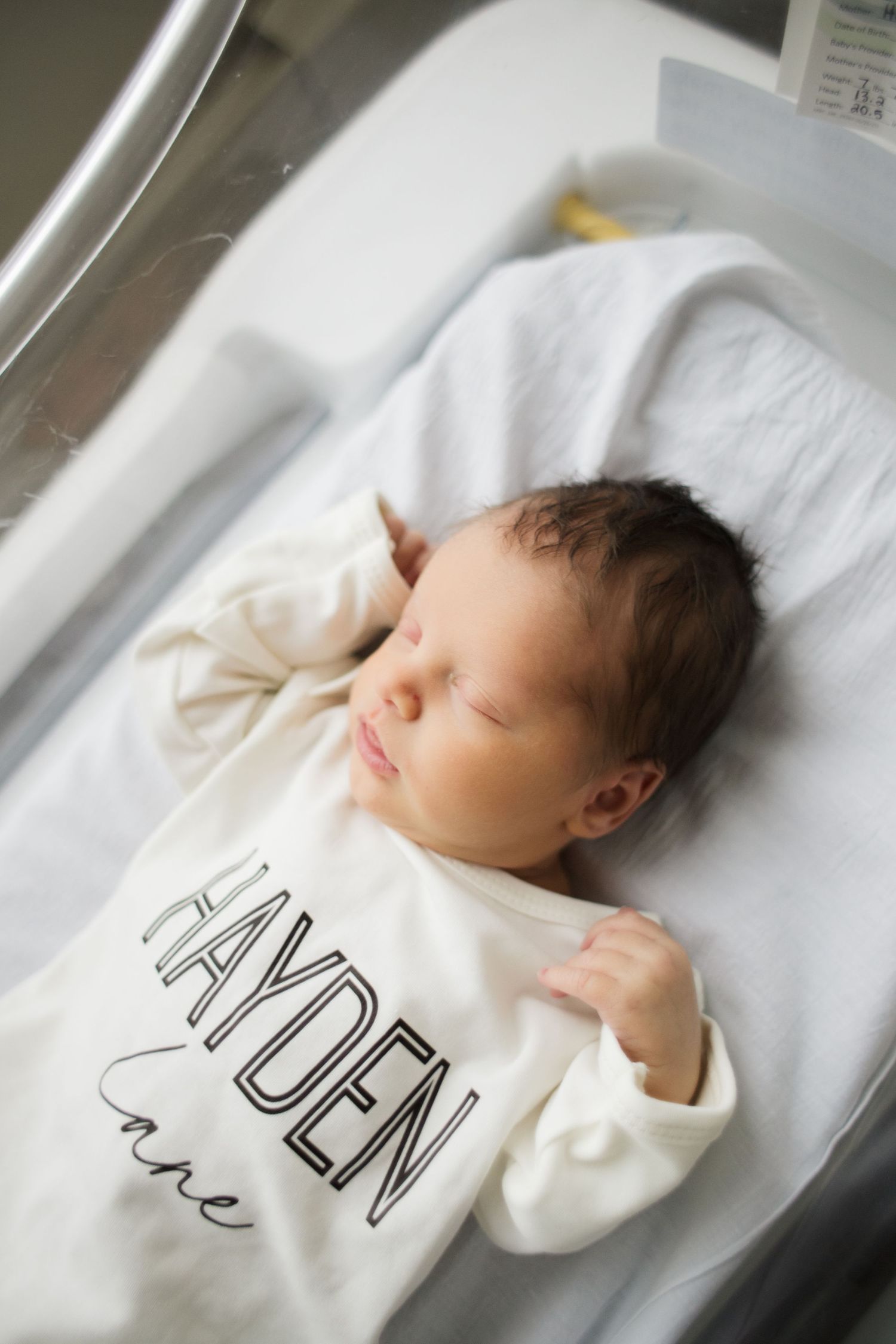 A sleeping infant wearing a white outfit lies peacefully on white bedding in a four-part photo sequence.
