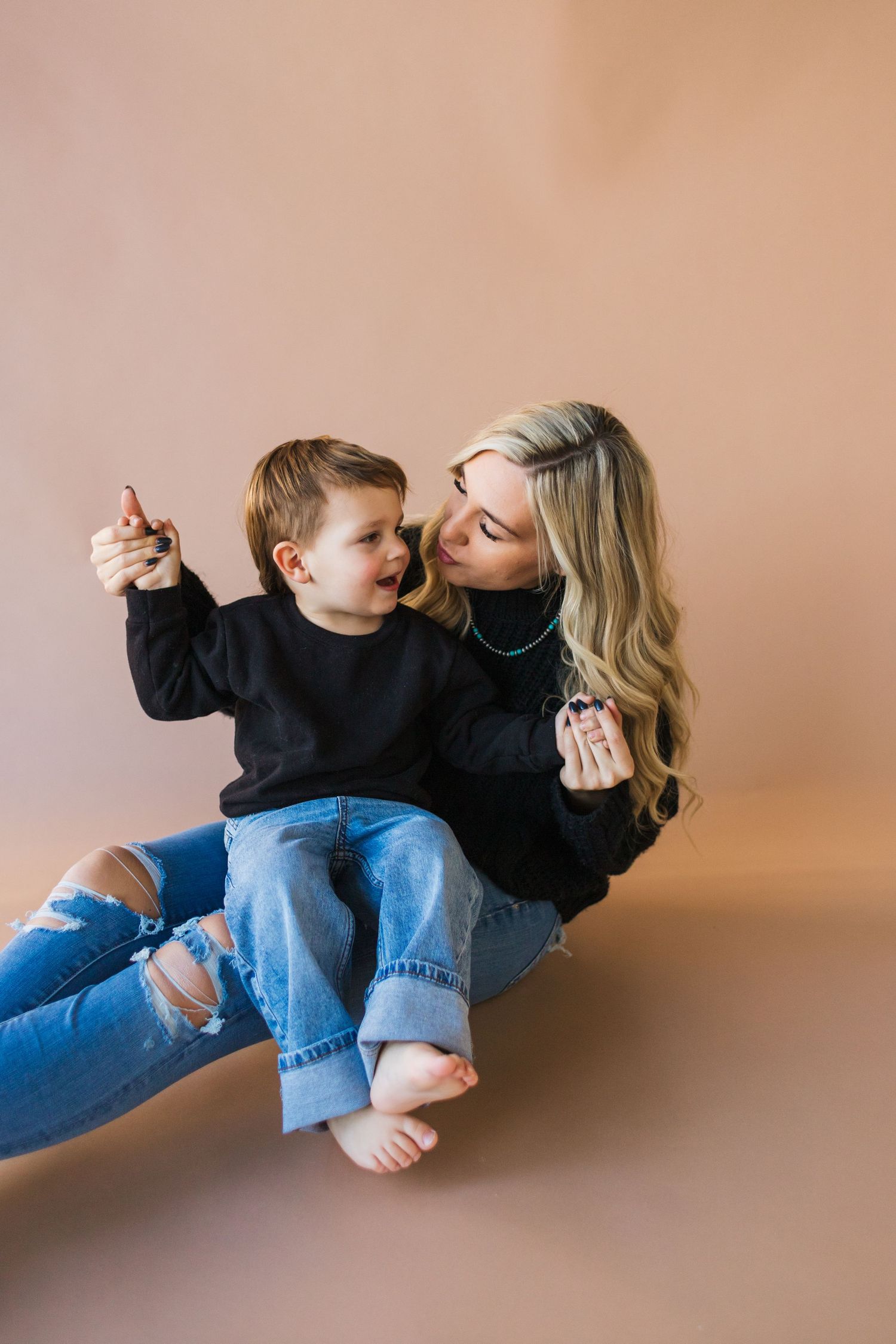 Mother and child pose playfully together in matching outfits on brown background.