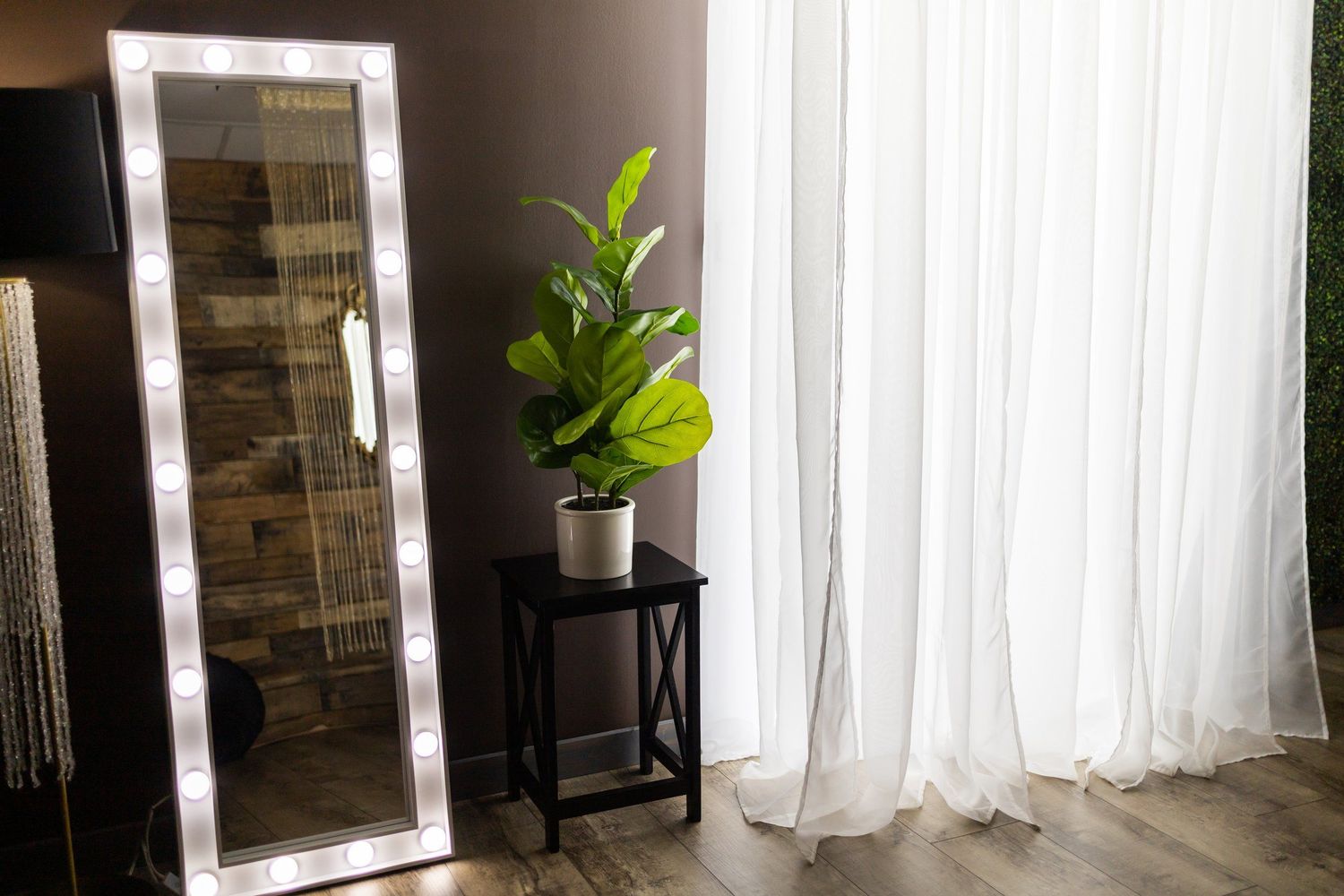 Minimalist room interior with LED mirror, white curtains, and potted plant on stand.
