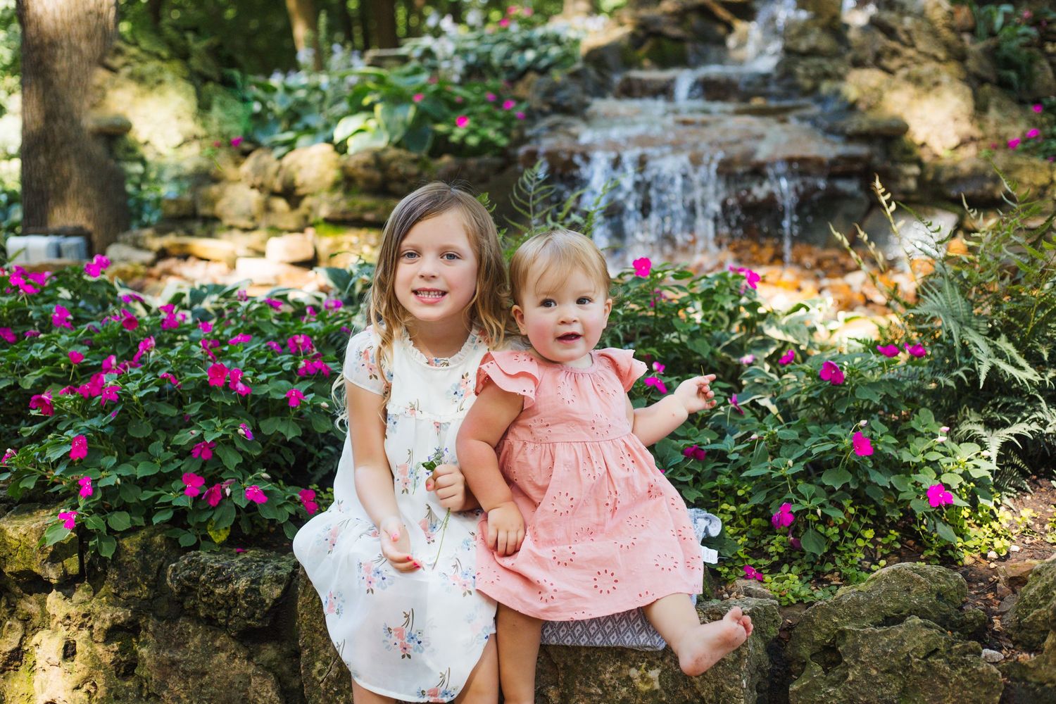 Family poses together on grassy hillside with pink flowers in summer garden setting.