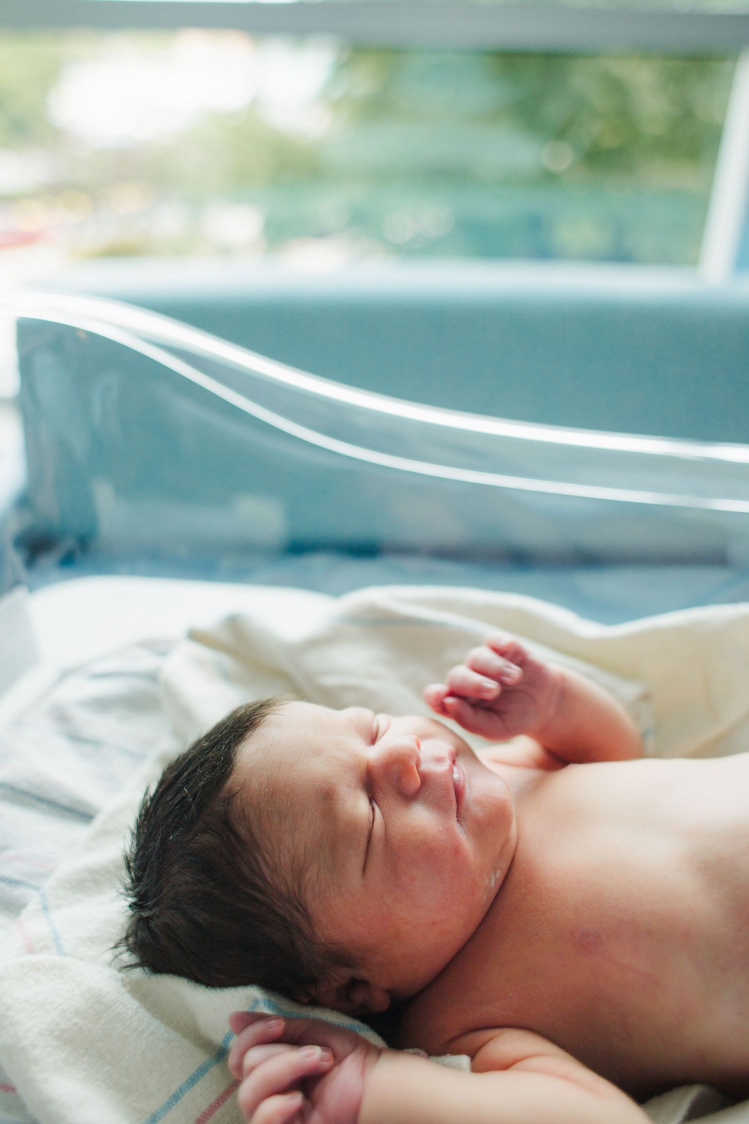 A newborn baby sleeping peacefully on soft white bedding in natural light.