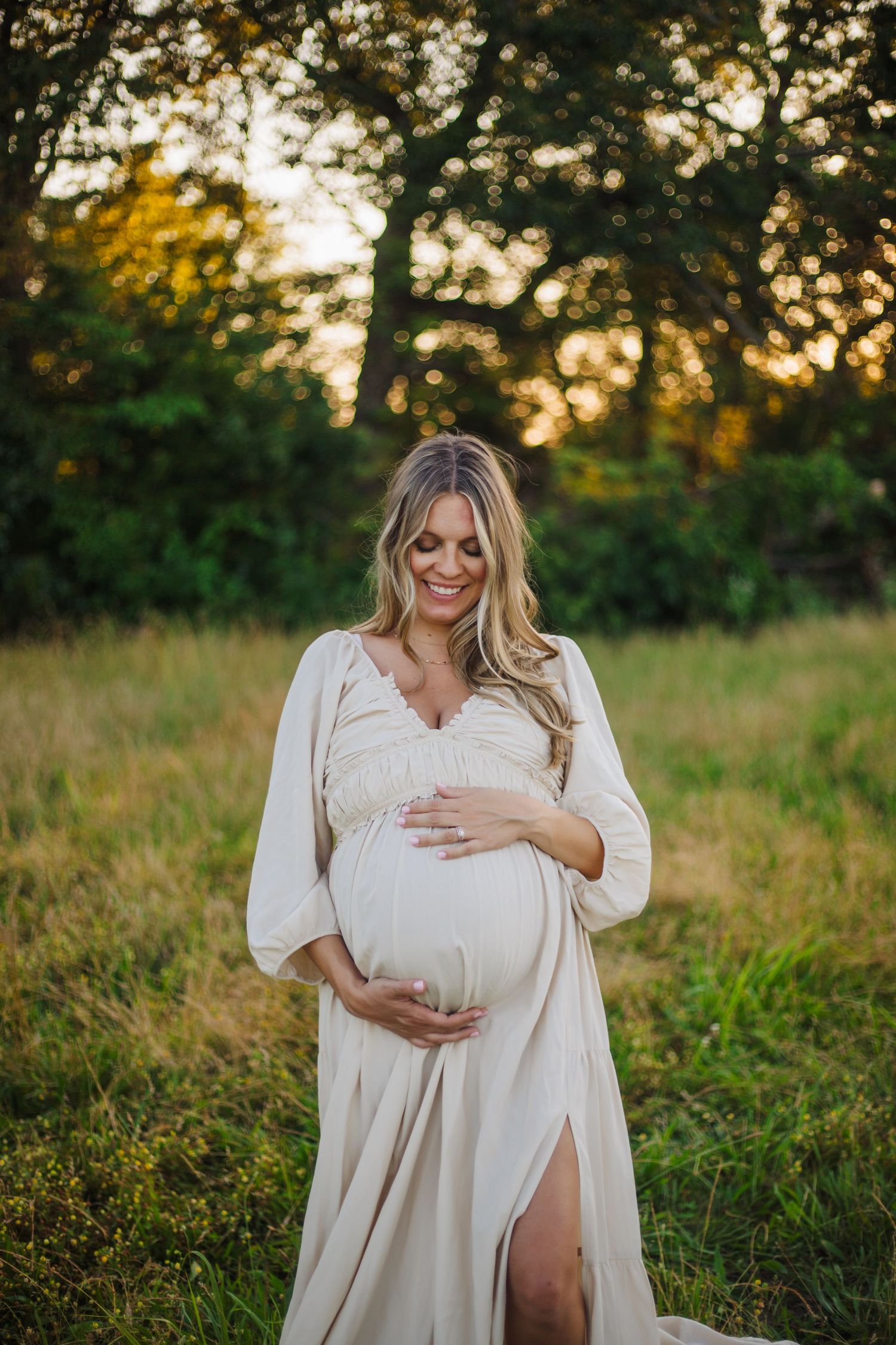 Elegant white maternity dress photographed in natural outdoor setting at golden hour.