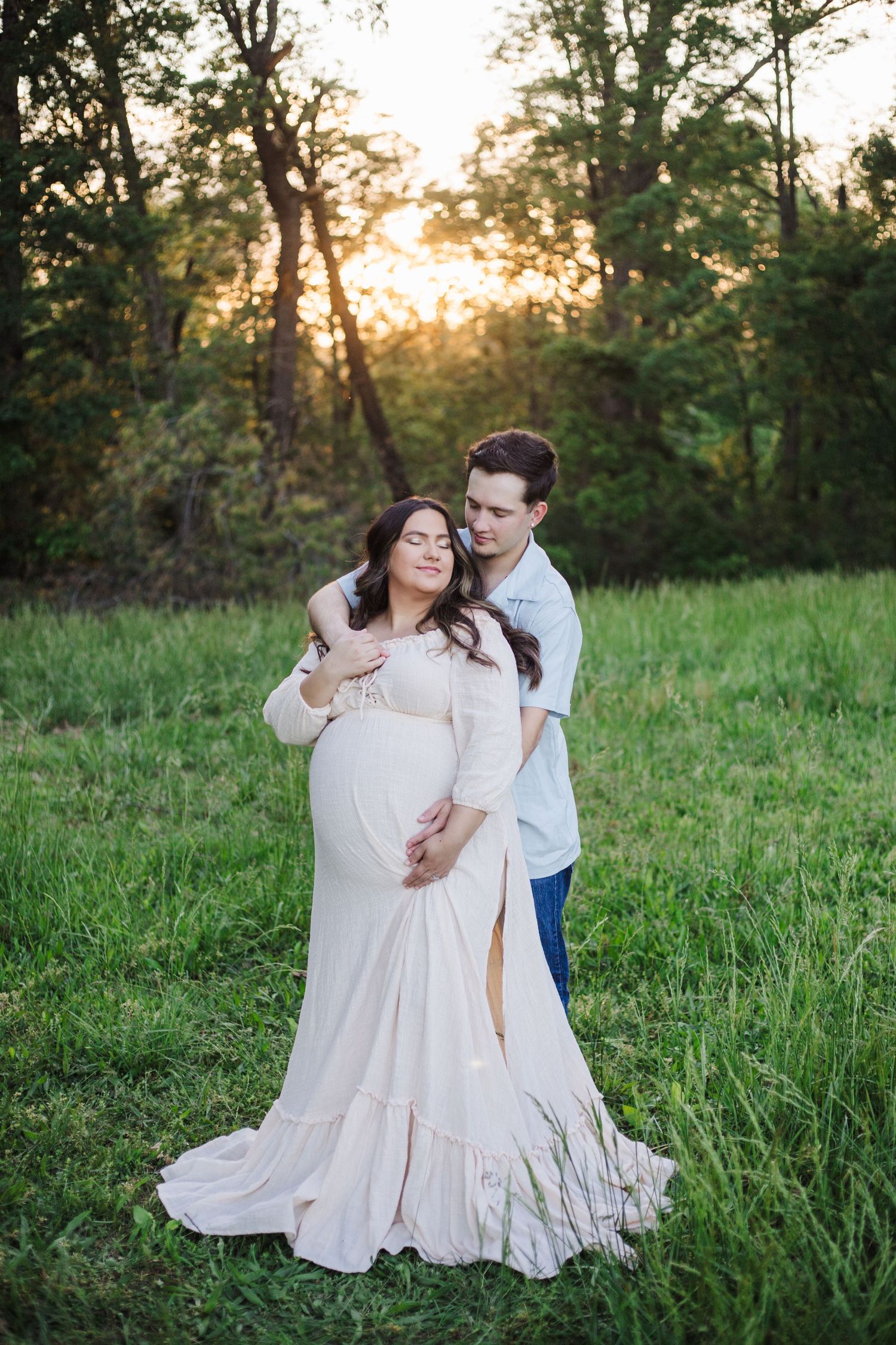 Romantic couple in white outfits embracing on grassy field during sunset.