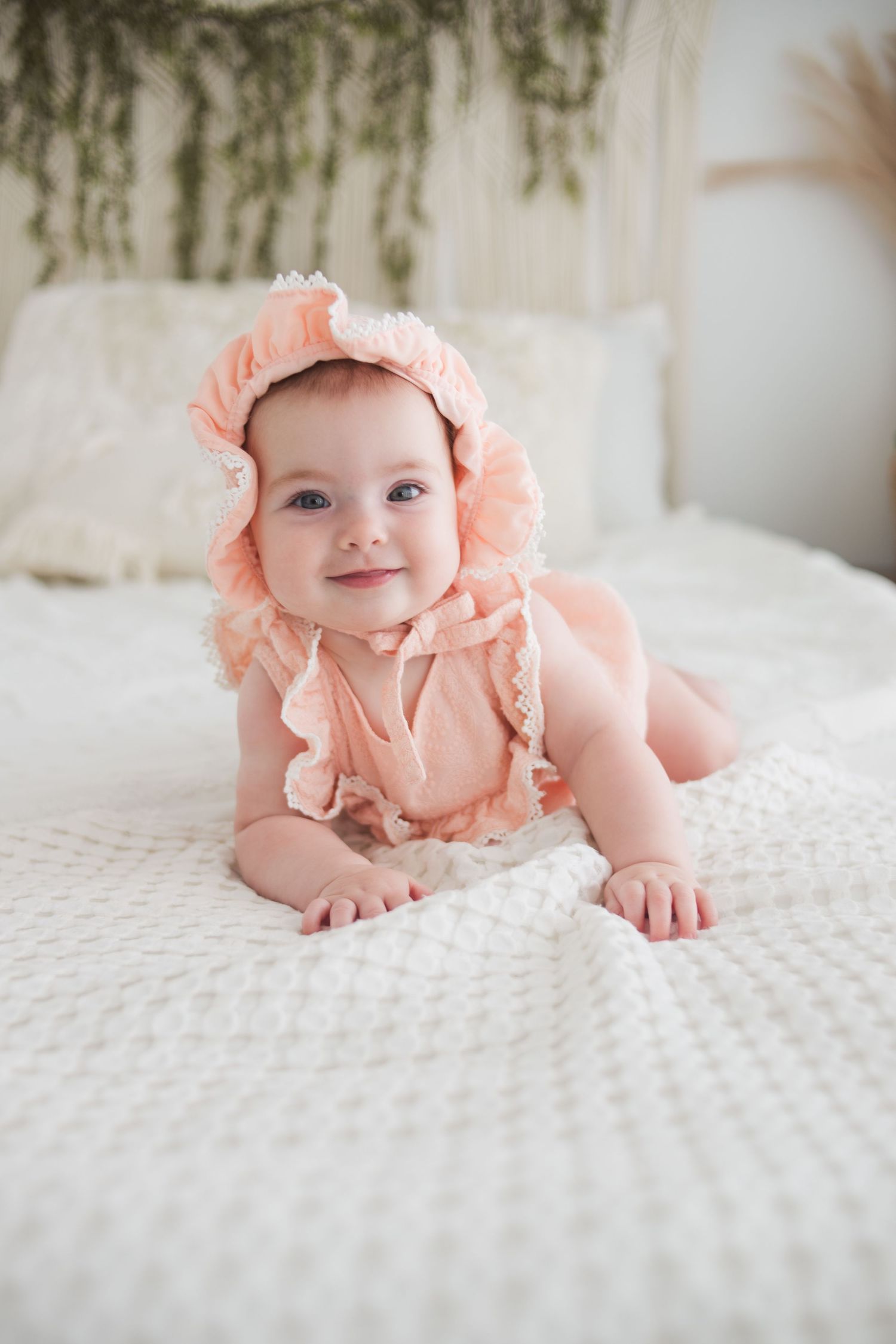 Sweet baby wearing a pink ruffled outfit lying on white textured bedding in a series of photos.