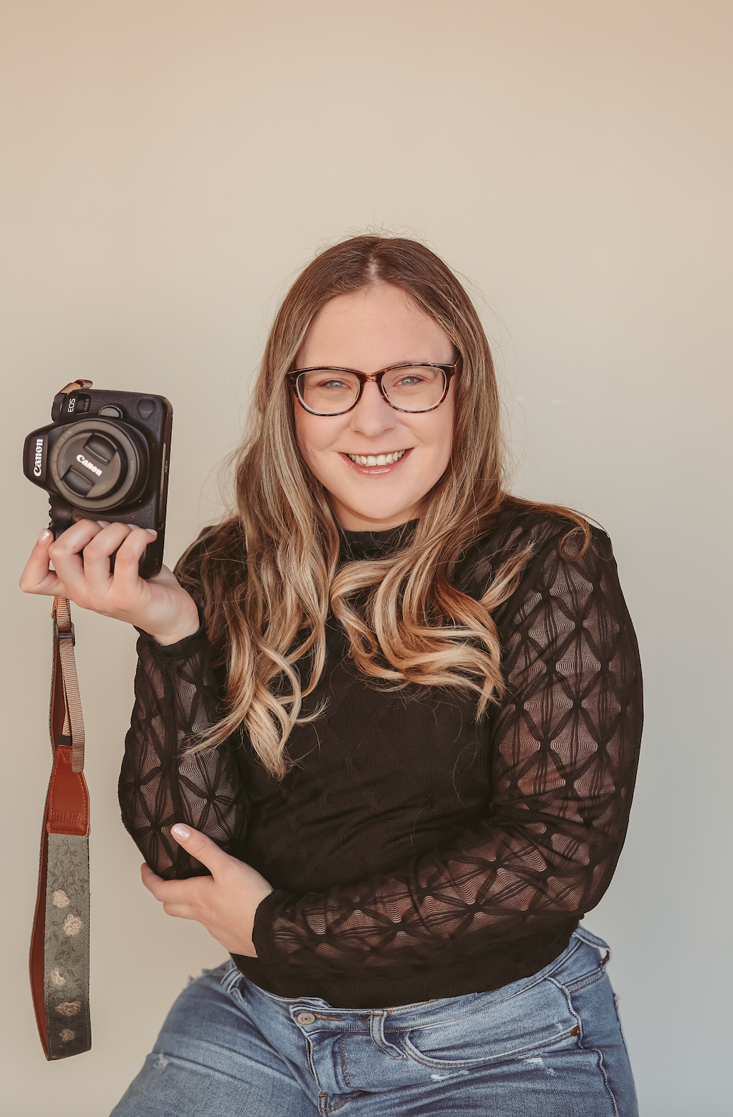 Portrait of photographer displaying vintage camera while wearing black lace top.