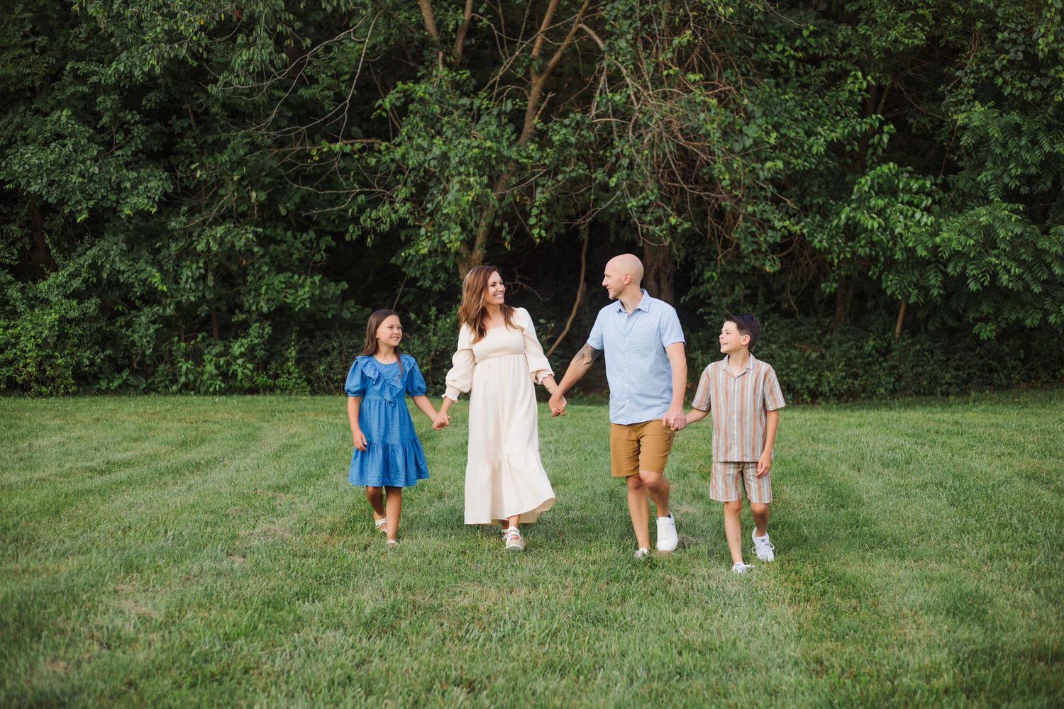 A family walks together hand in hand through a grassy field on a summer evening.