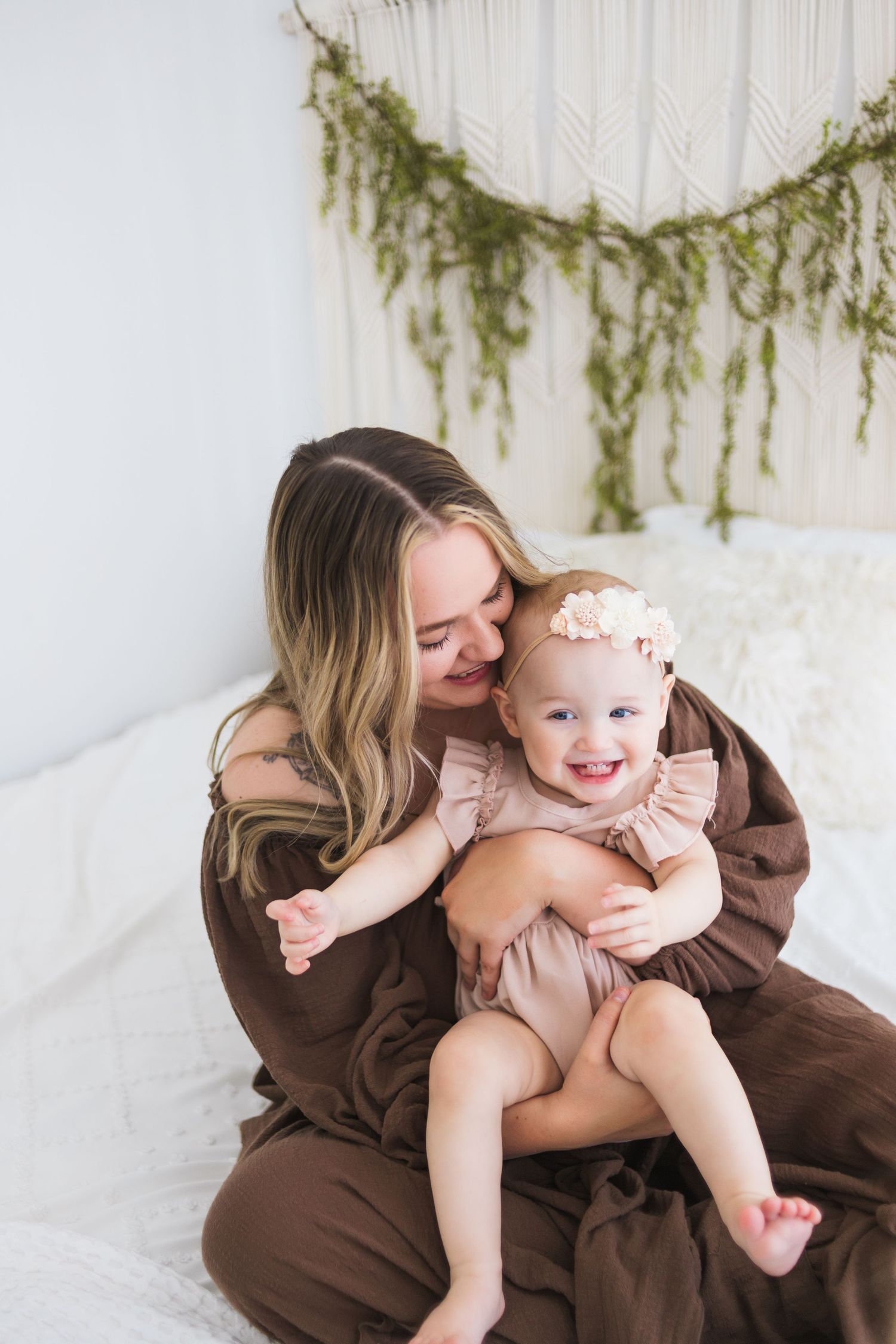 A tender moment captured between parent and baby with decorative greenery garland on white wall.