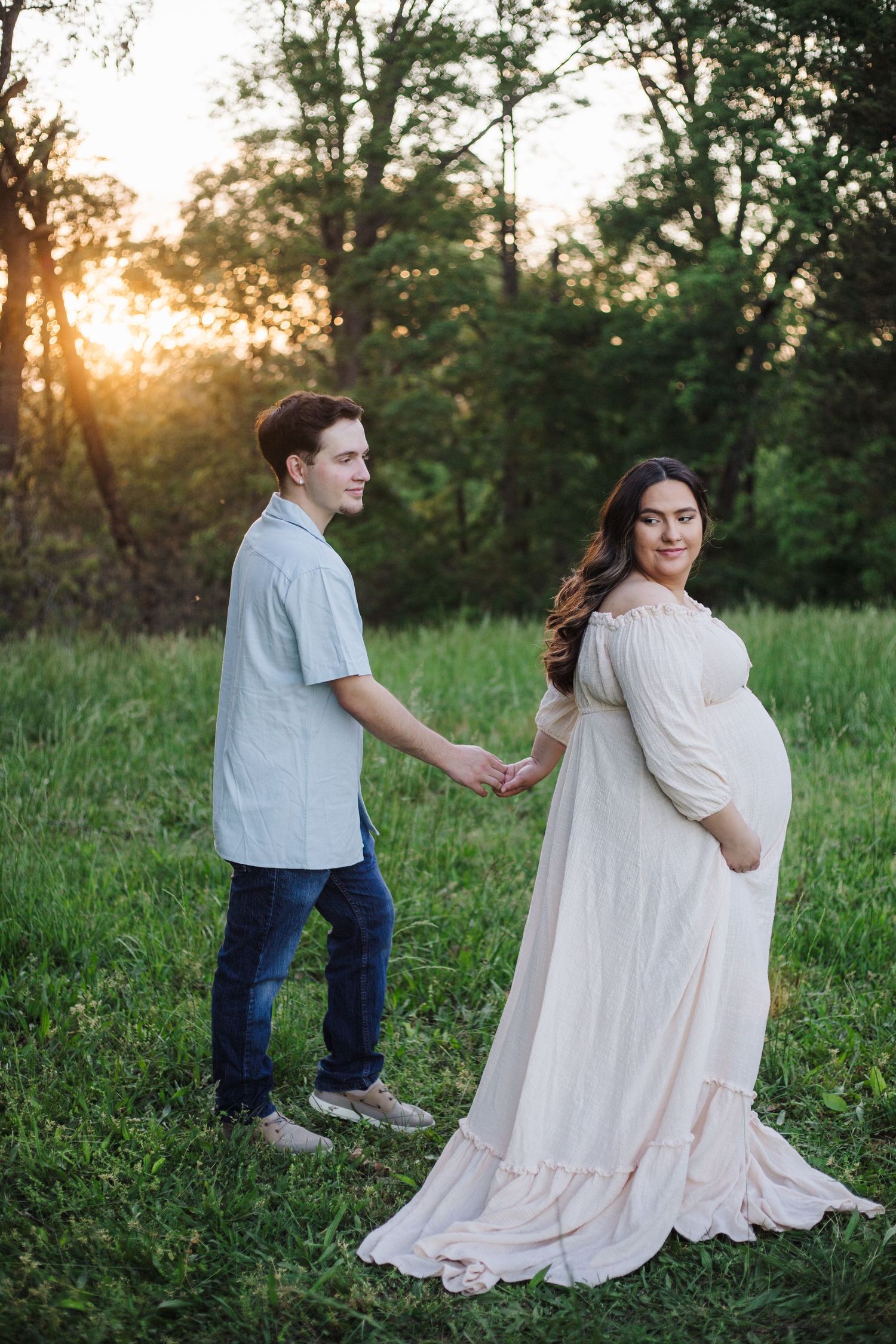 Family members interacting playfully in a sunlit meadow wearing light colored clothing.
