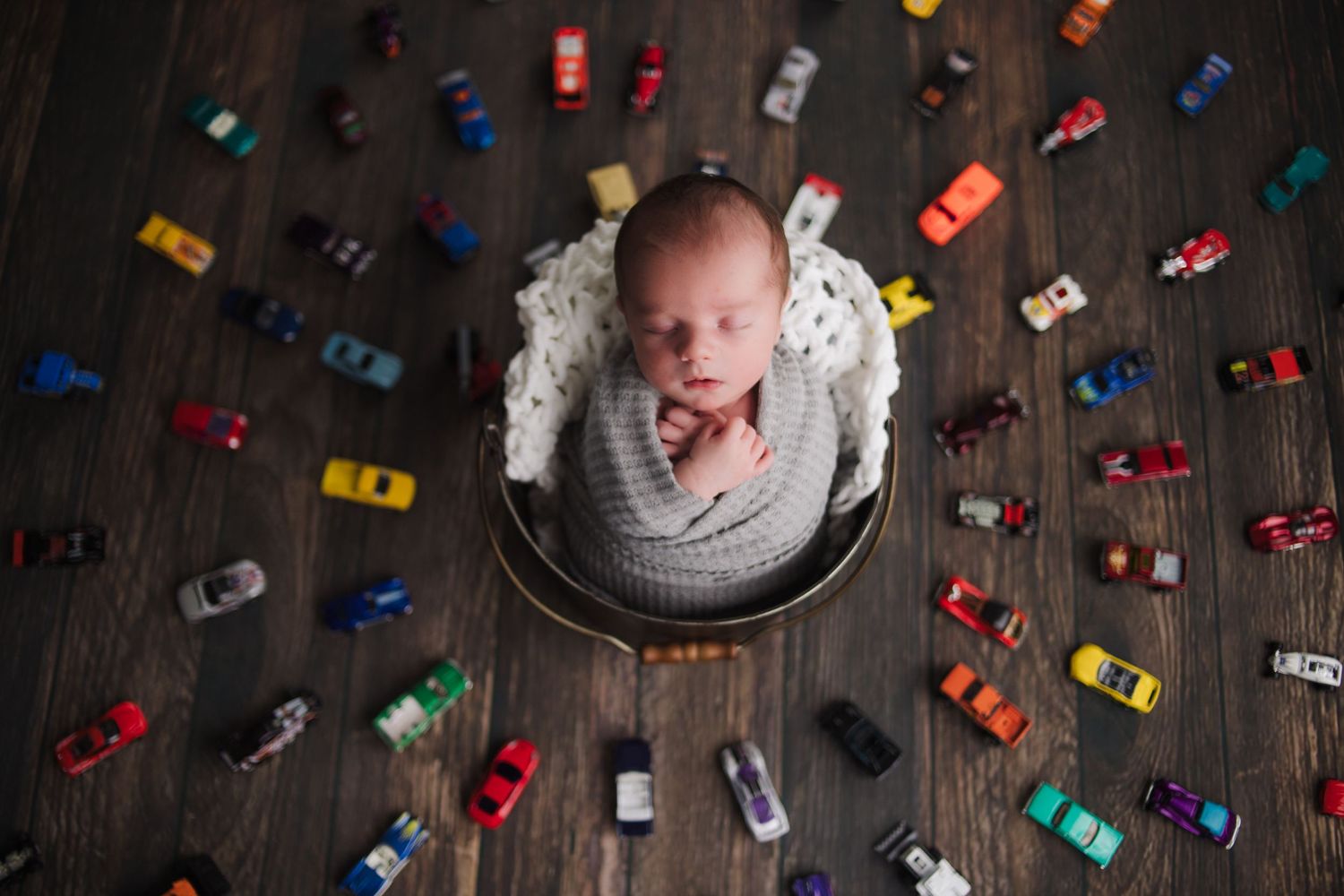 creative newborn baby portrait surrounded by toy cars in studio setup