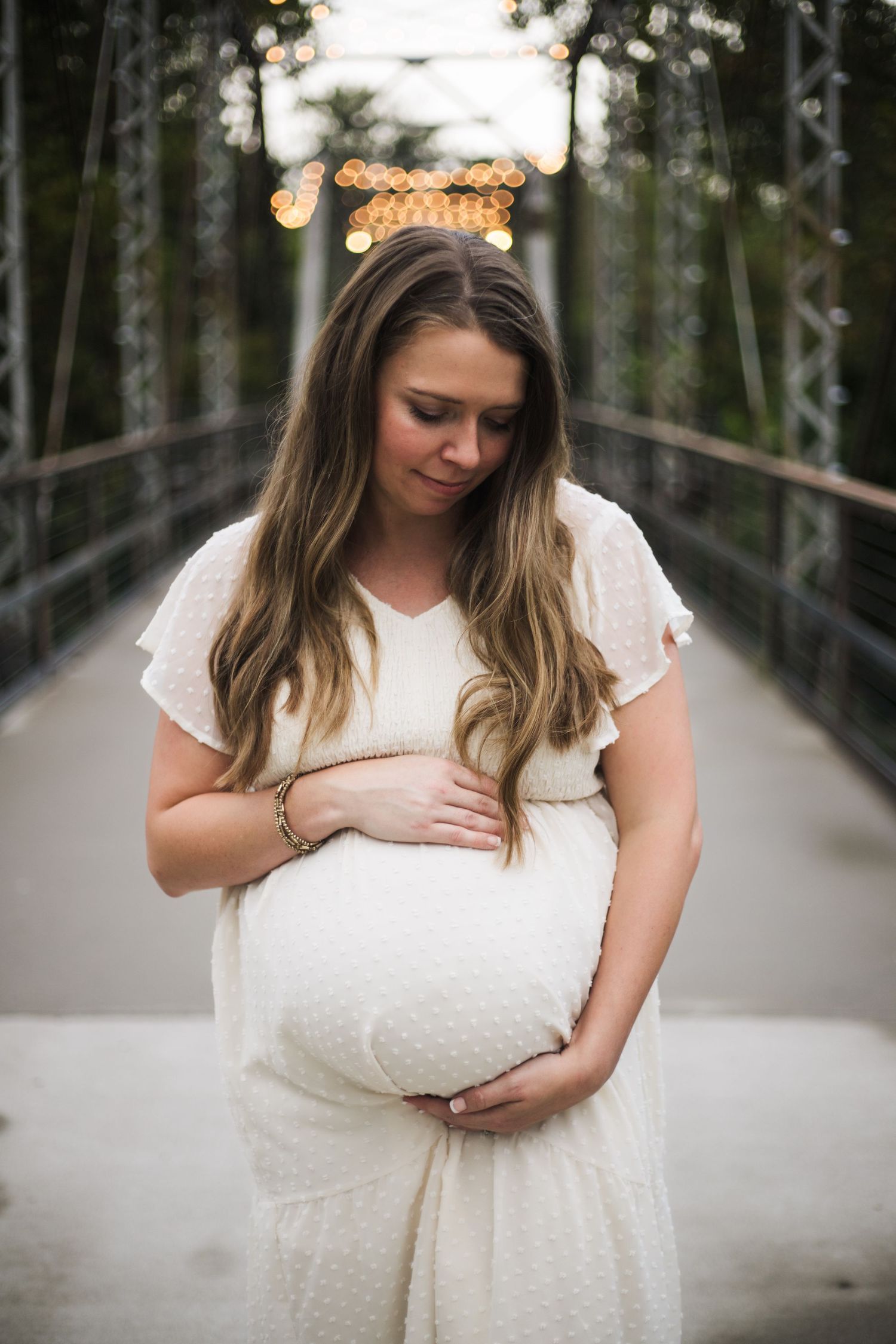 A series of maternity photos showing a woman in a white lace dress standing on a wooden bridge in a forest setting.