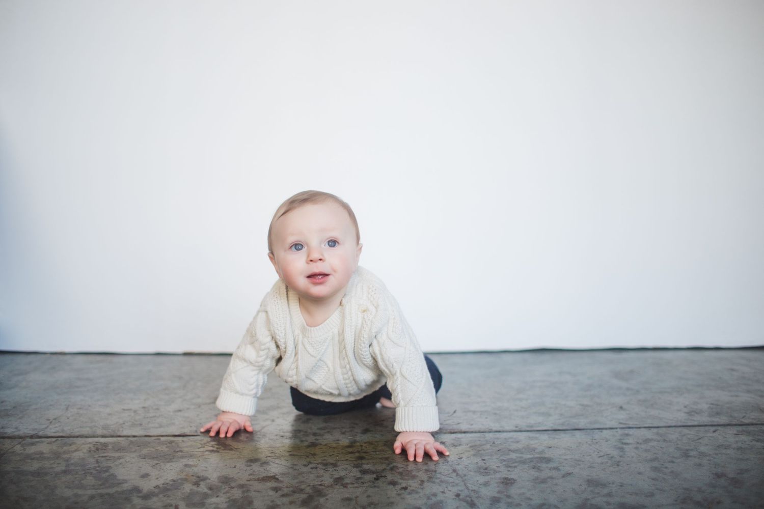 A series of progressive photos showing a baby crawling across a light gray floor against a white wall.
