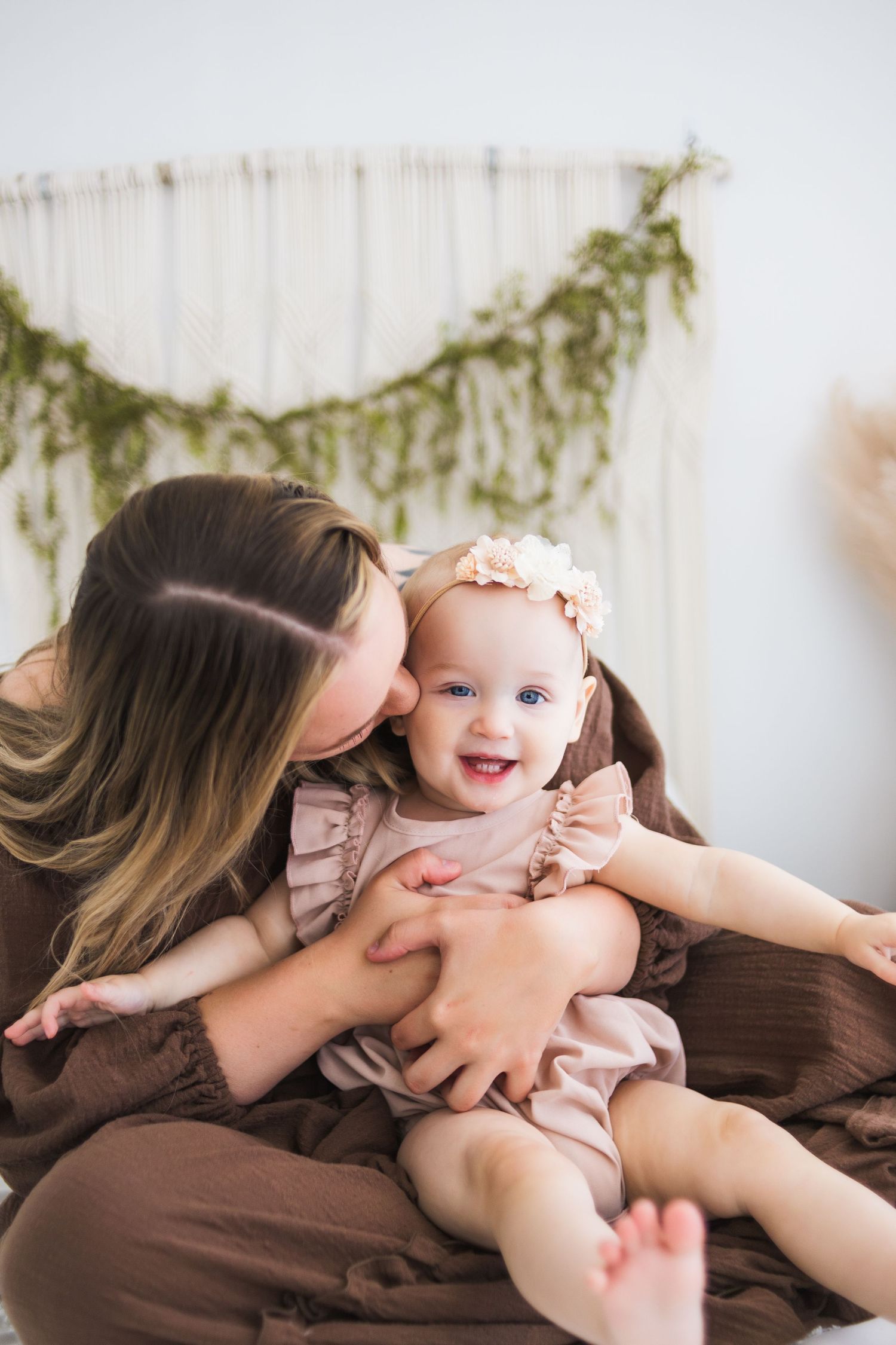 Joyful interaction between parent and smiling baby in brown dress against white background.