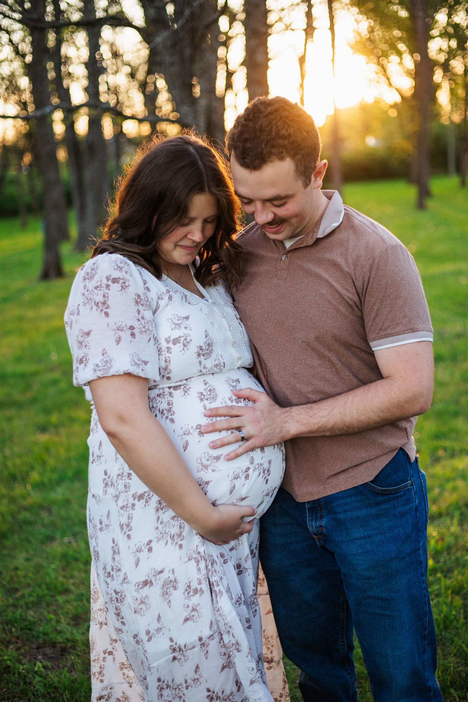 Expecting couple sharing tender moment in sunlit forest setting.