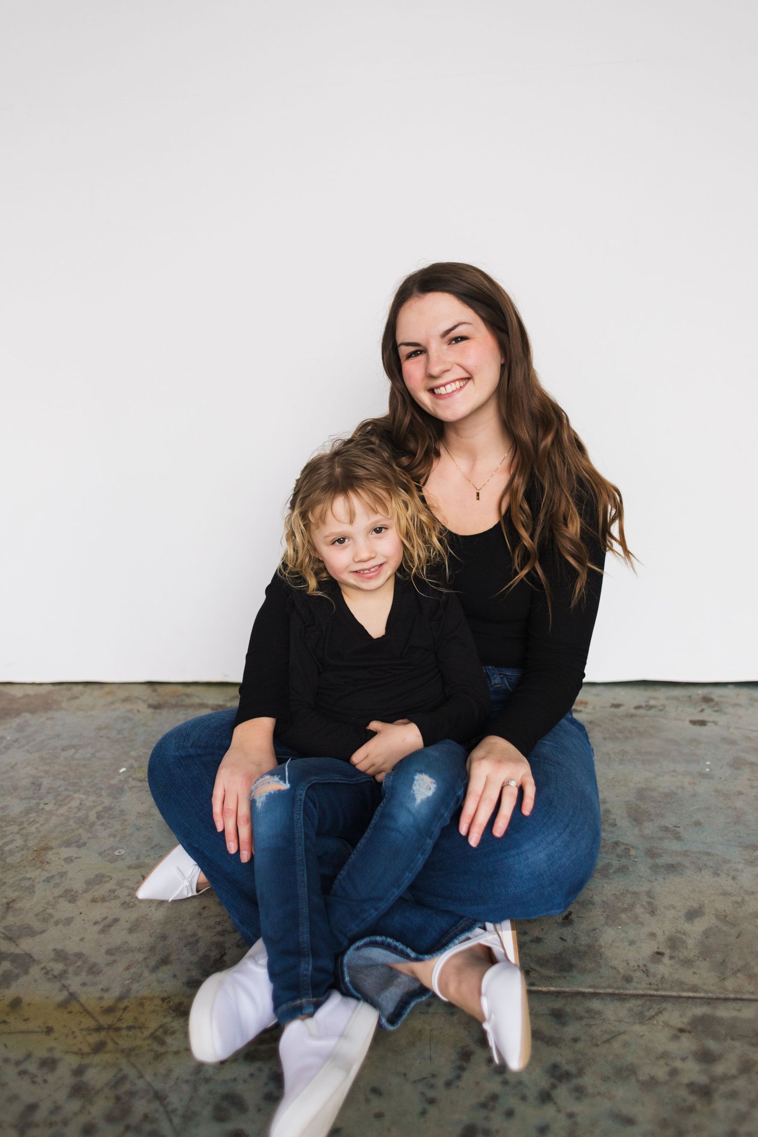 Mother and child sit together on floor wearing matching black tops and jeans.
