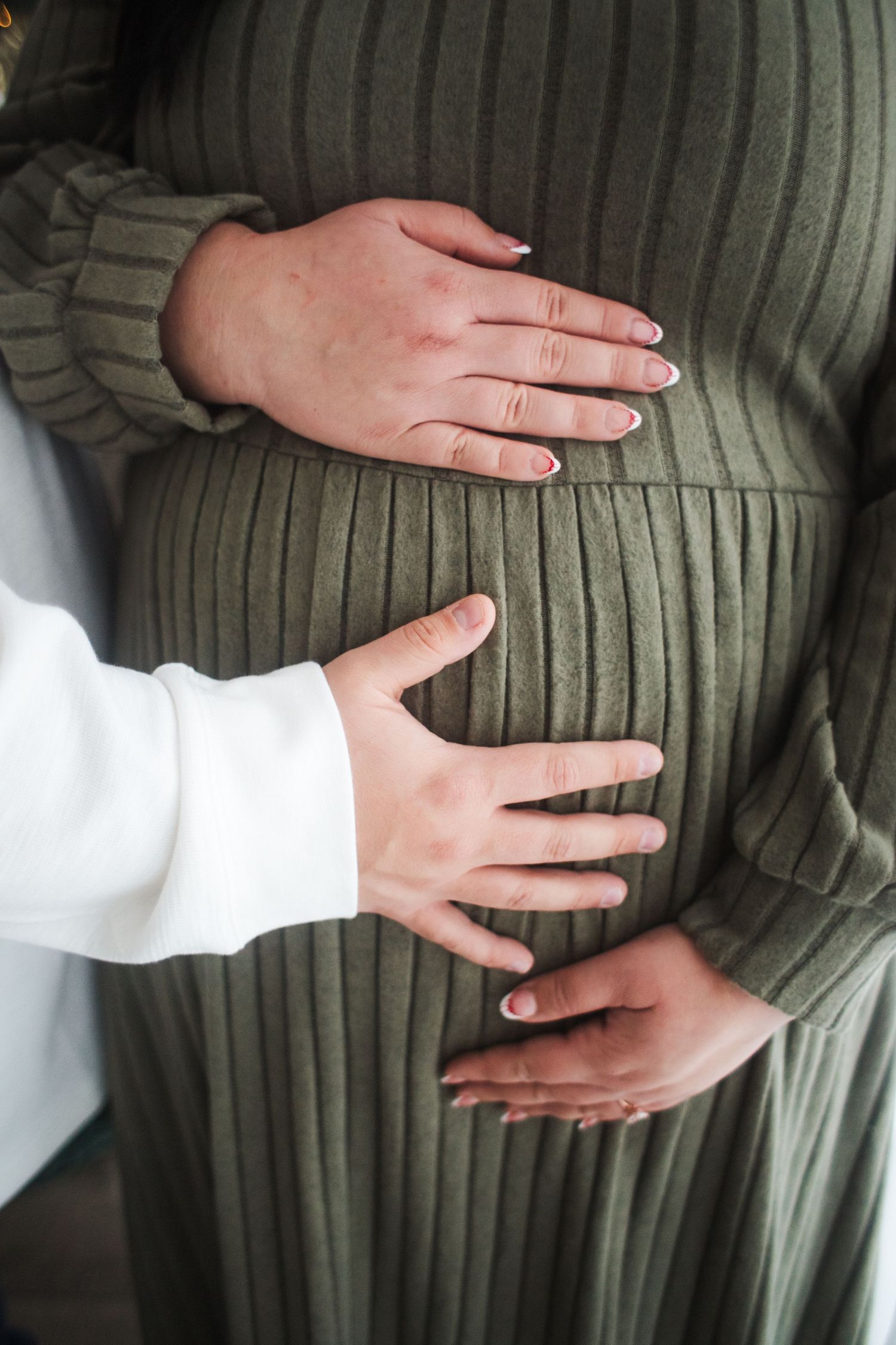 Four sequential photos showing hands gently placed on a pregnant belly wearing a green sweater.