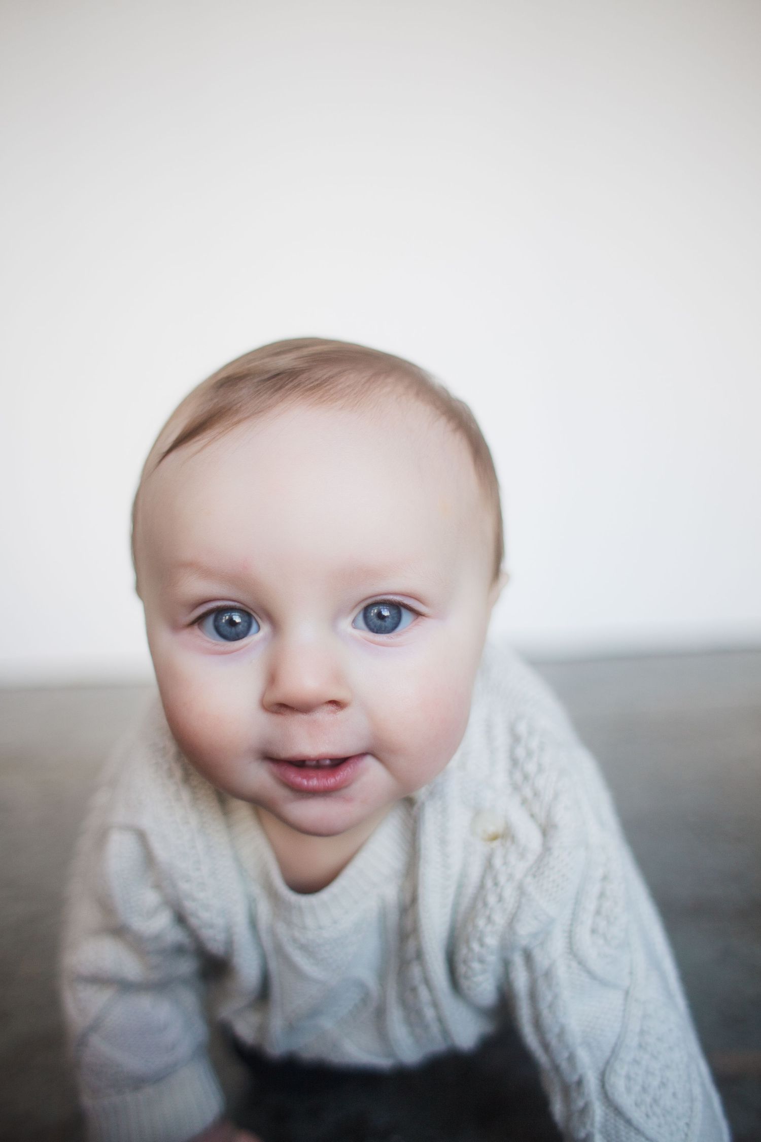 A sequence of four photos showing a baby in a white knit sweater expressing different emotions and expressions.