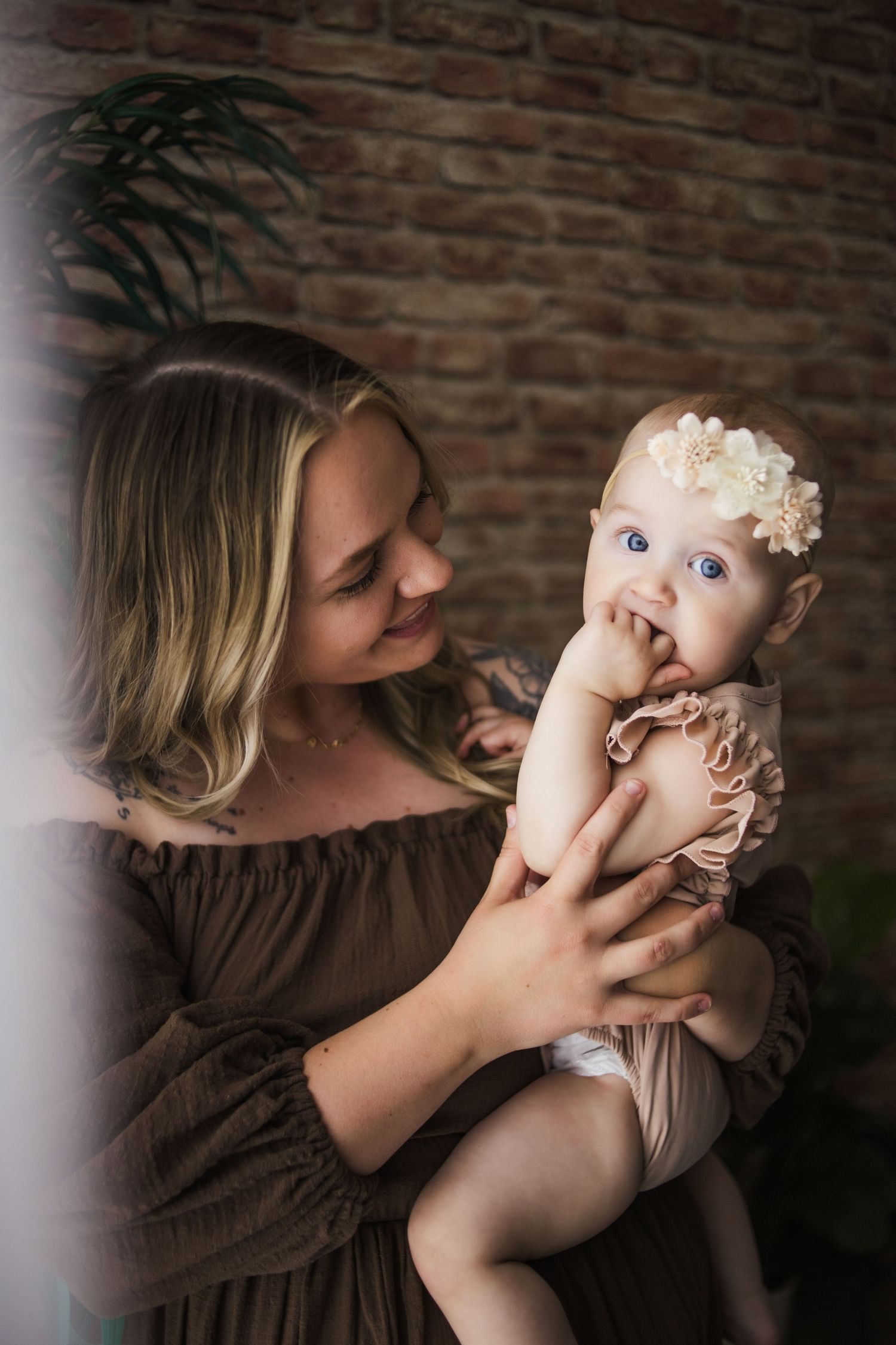 Intimate portrait against brick wall captures tender moment between parent and baby in neutral tones.