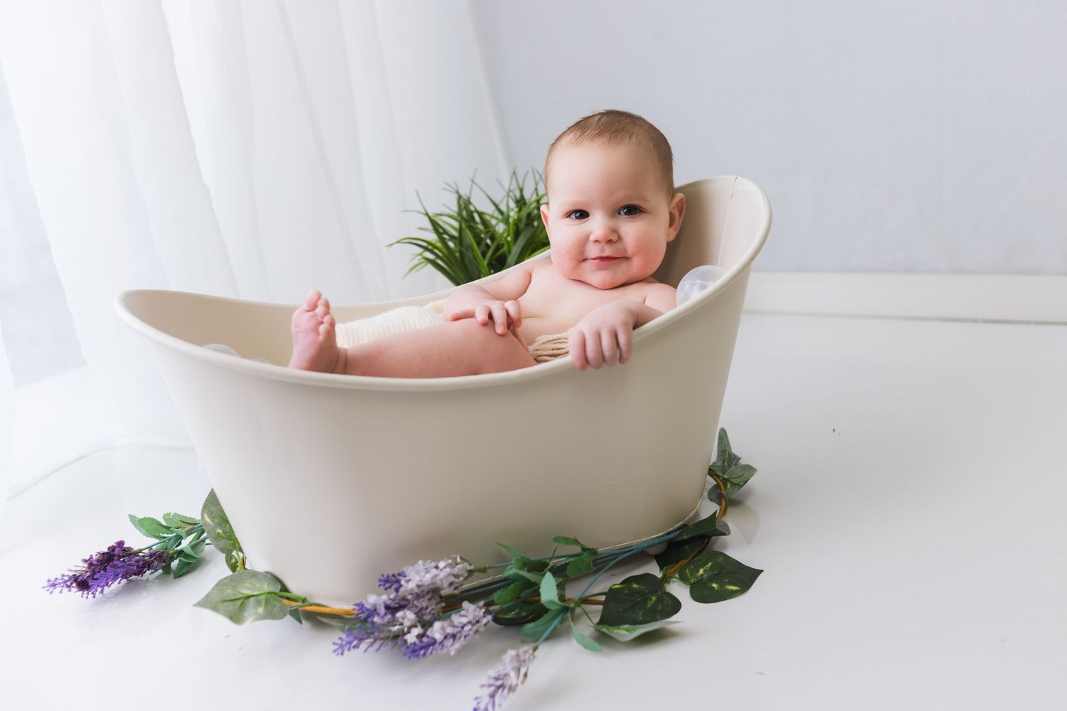 Minimalist bath photography with white tub and purple flowers against light background.
