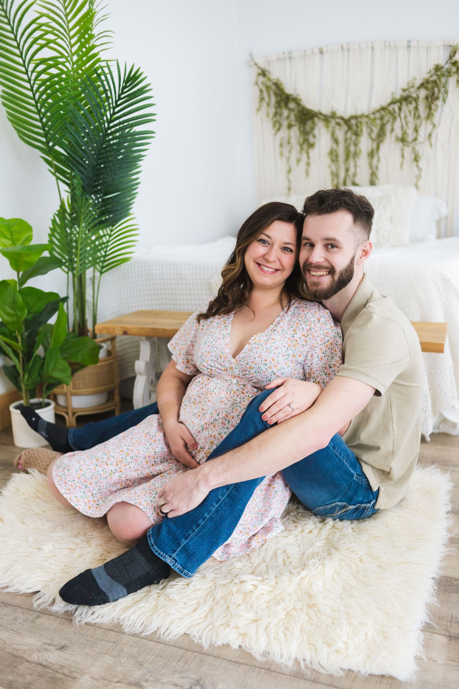 A couple embraces on a fluffy white rug during their maternity photoshoot.