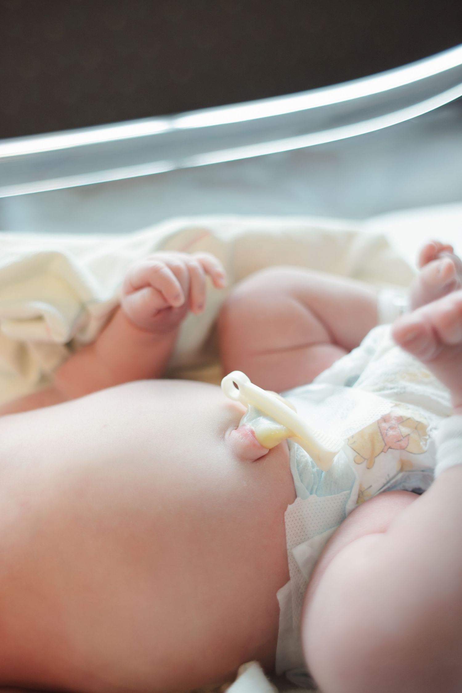 A sleeping infant lies peacefully in a white diaper against a soft white background.