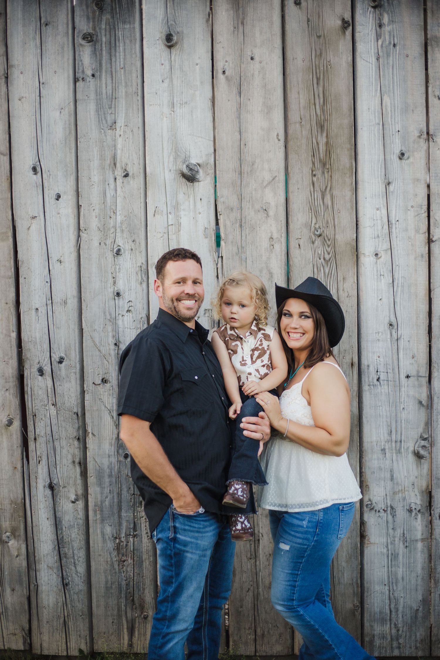 A family poses together for a portrait against a weathered wooden wall.