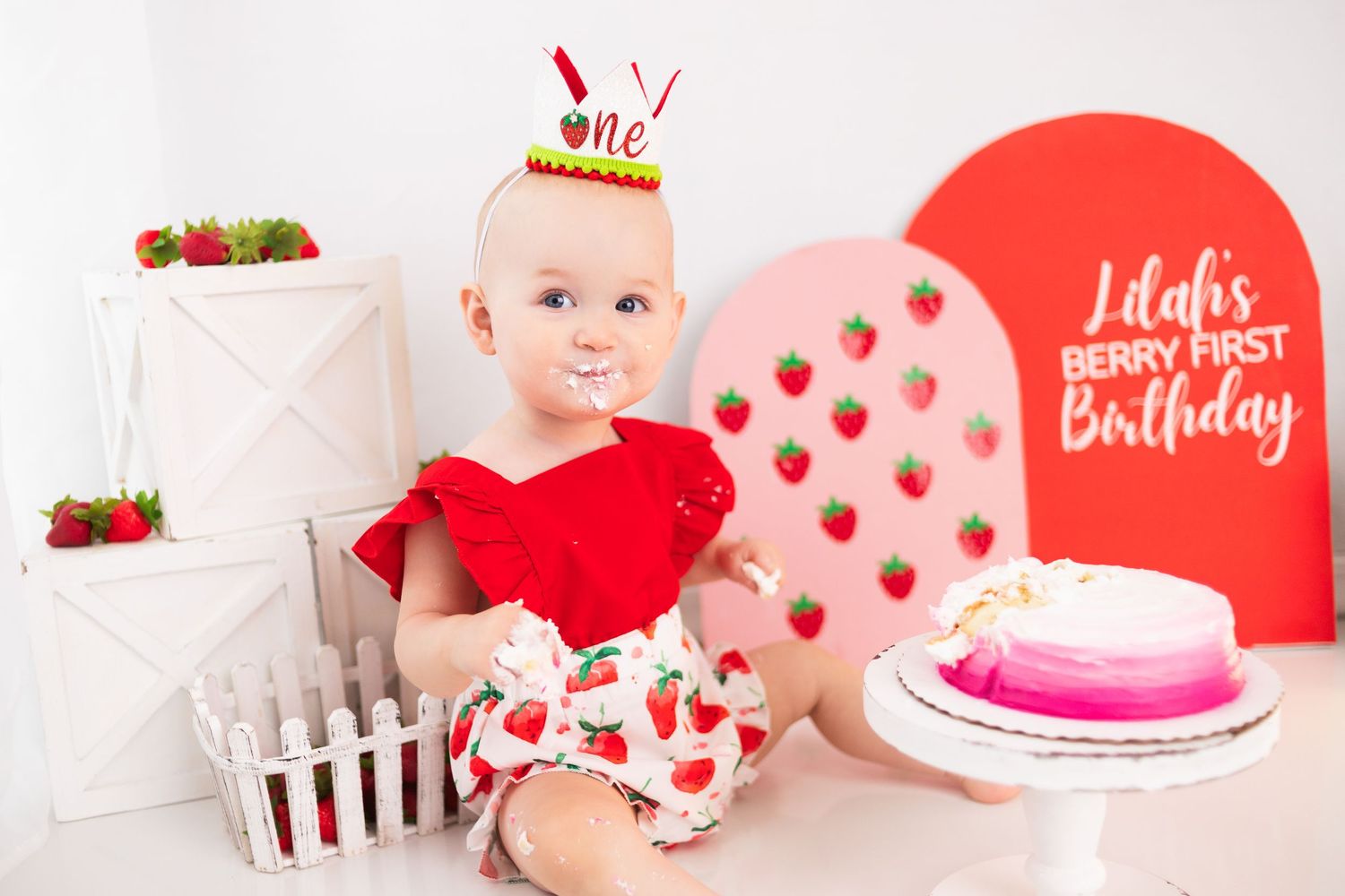 Red and white birthday setup with strawberry theme decorations and pink cake.