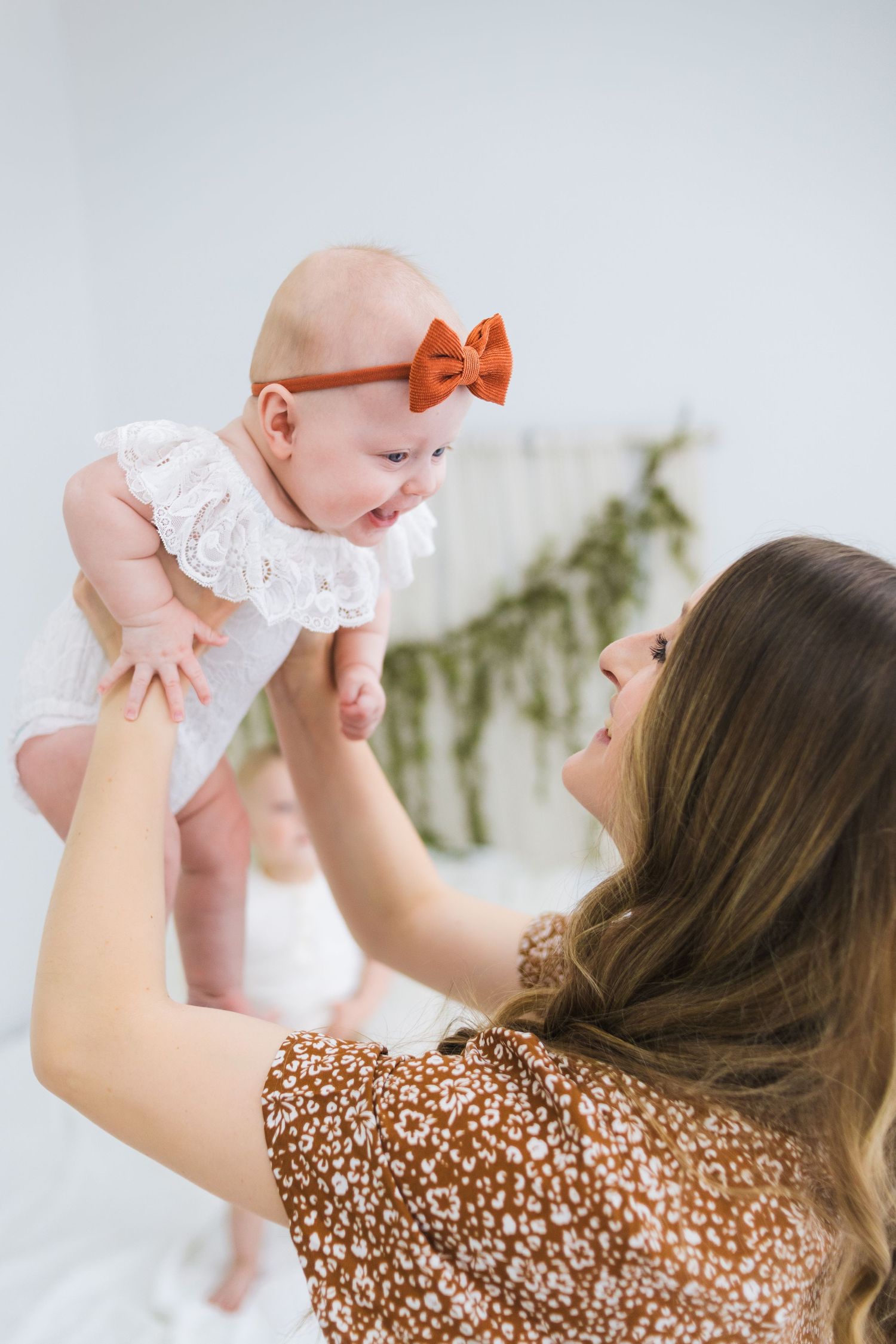 Joy-filled parenting moment as a baby in white with orange bow is lifted up playfully.